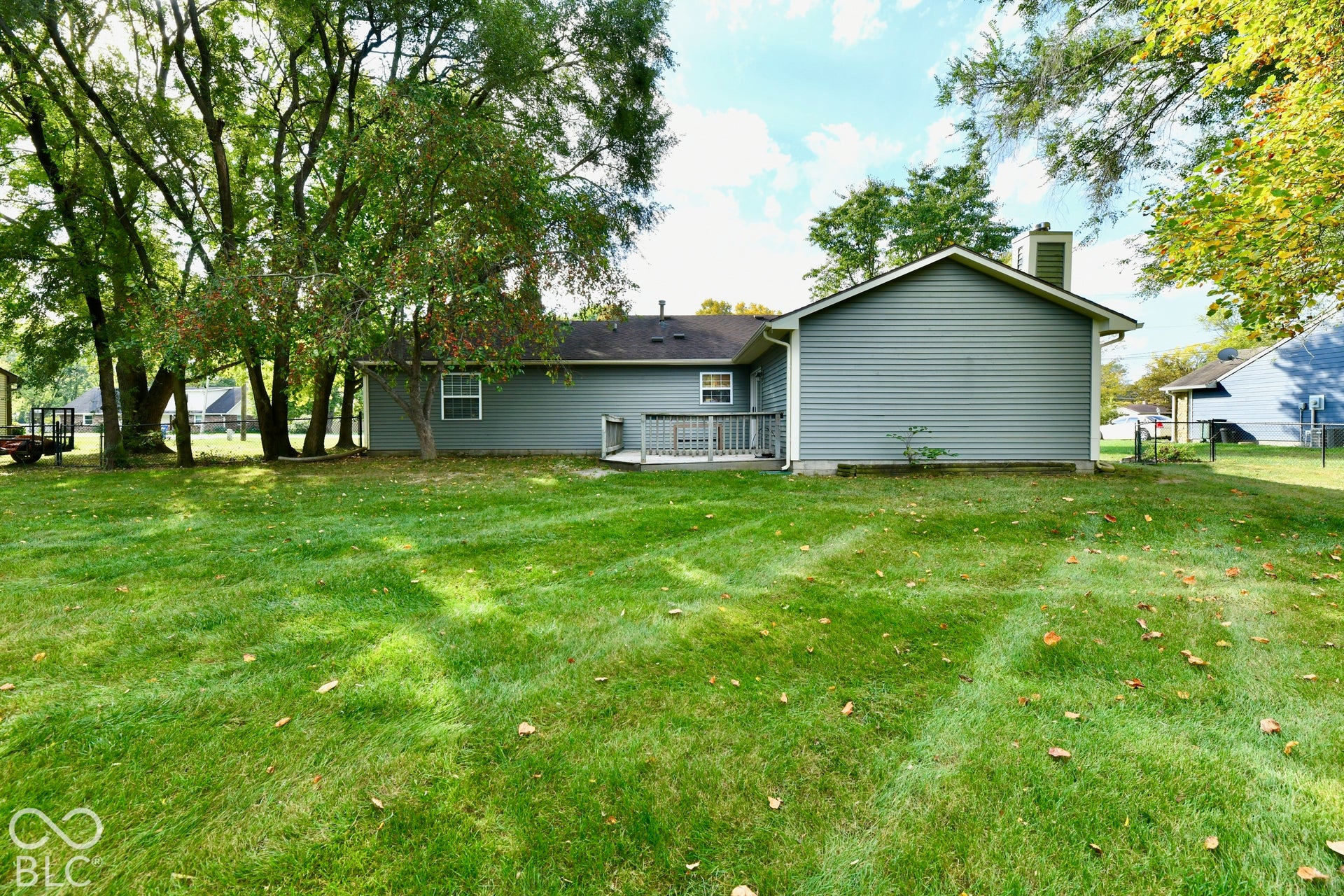 Expansive backyard featuring a sprawling lawn, mature trees, exterior horizontal siding, a chimney, and a raised wooden deck