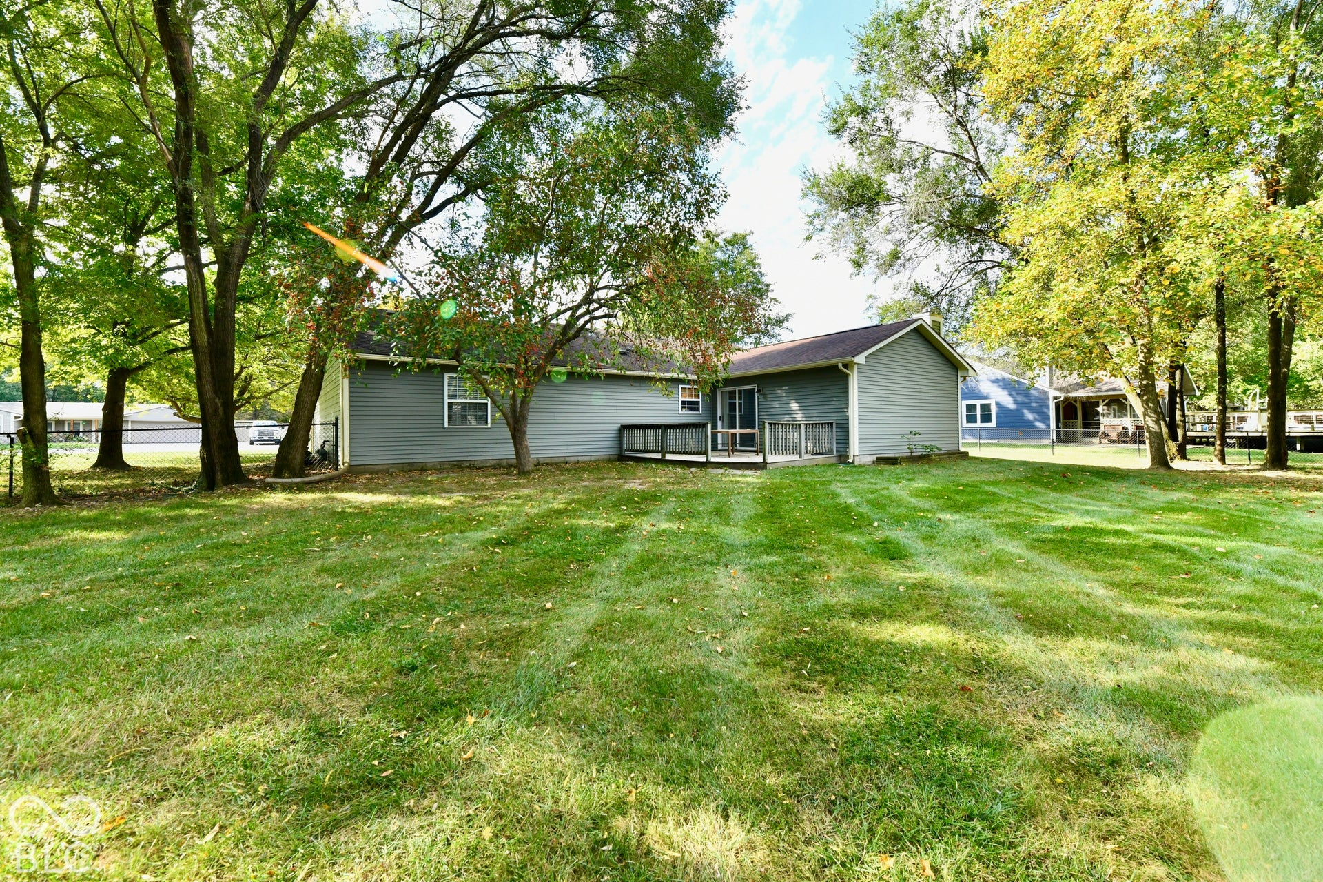 Expansive backyard featuring a large grass lawn, mature trees, and a wooden deck