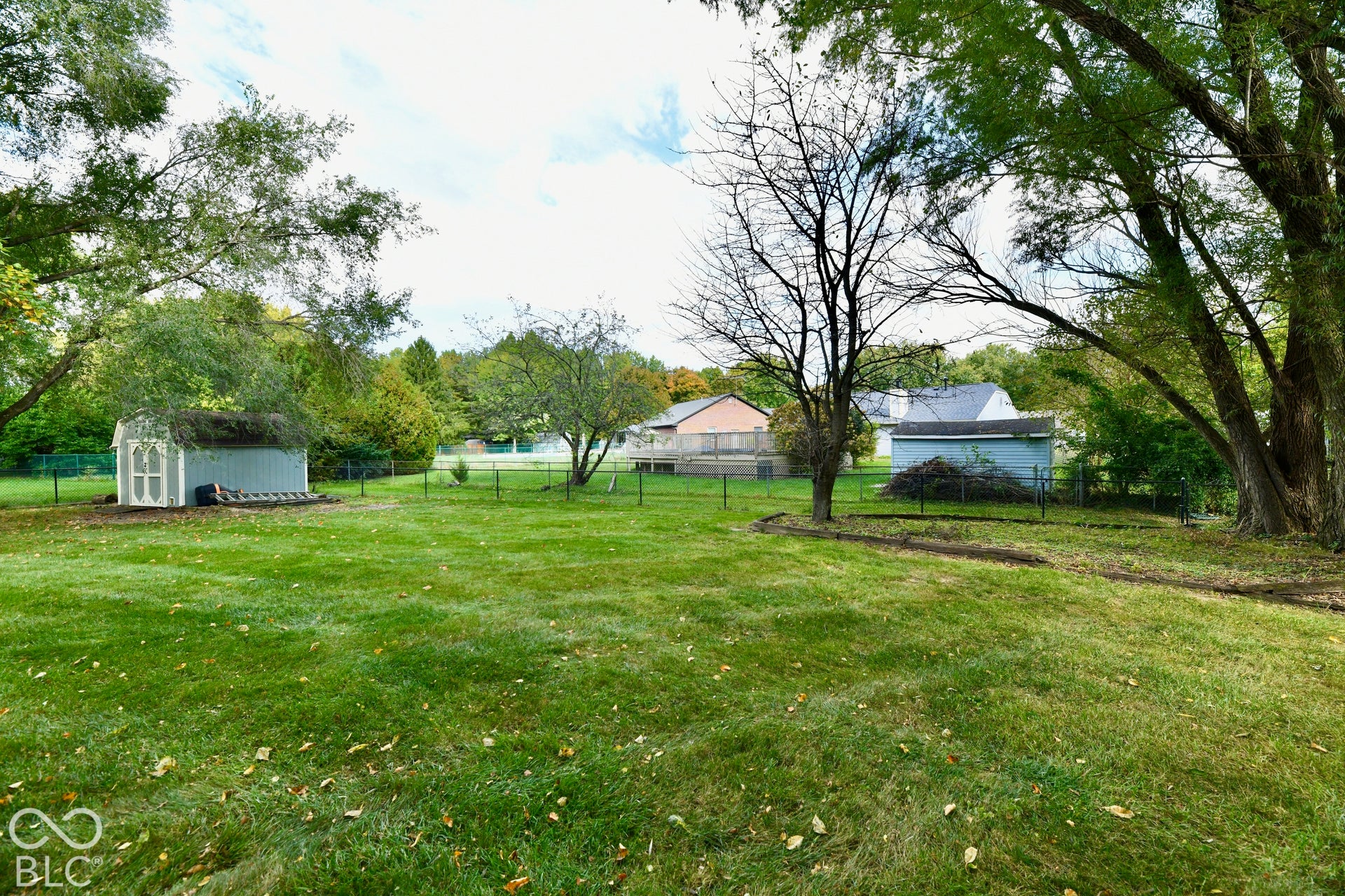 Expansive backyard featuring a large grass lawn, mature trees, perimeter fencing, and two detached storage structures