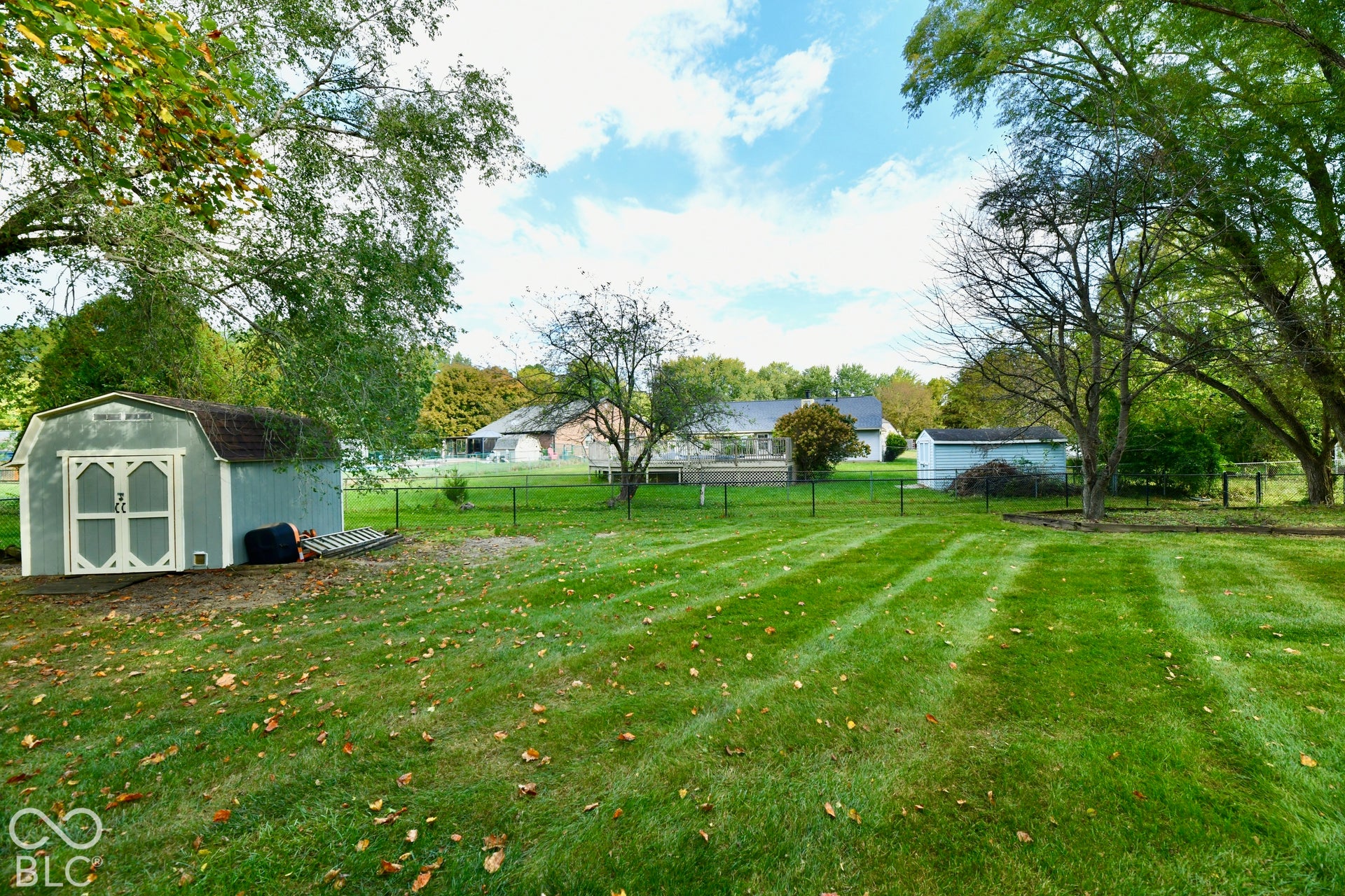 Expansive lawn featuring mature trees, perimeter fencing, and two storage sheds