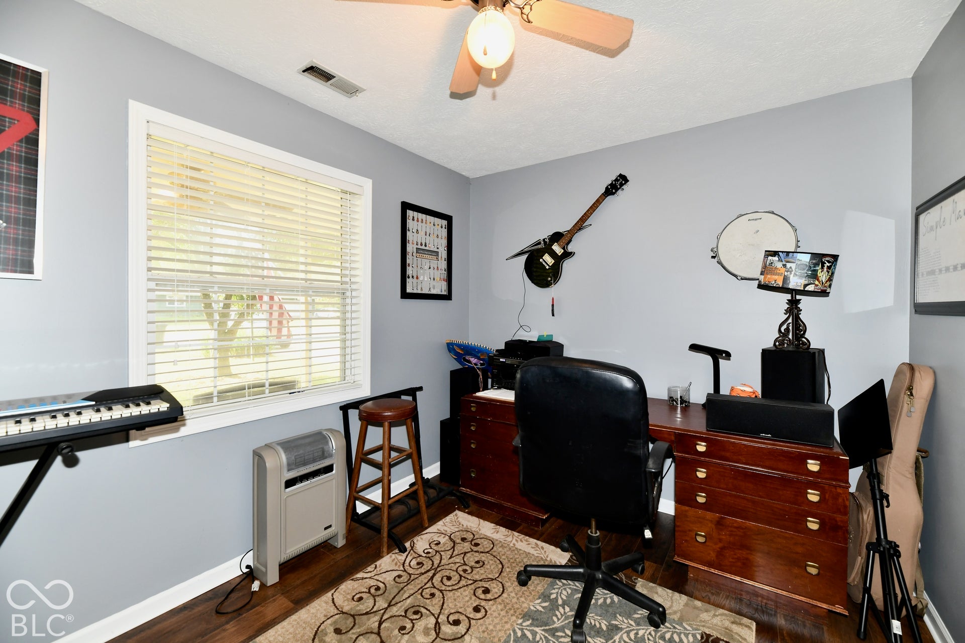 Neutral wall palette, wood-finish flooring, multi-pane window with horizontal blinds, and a ceiling-mounted light fixture with fan