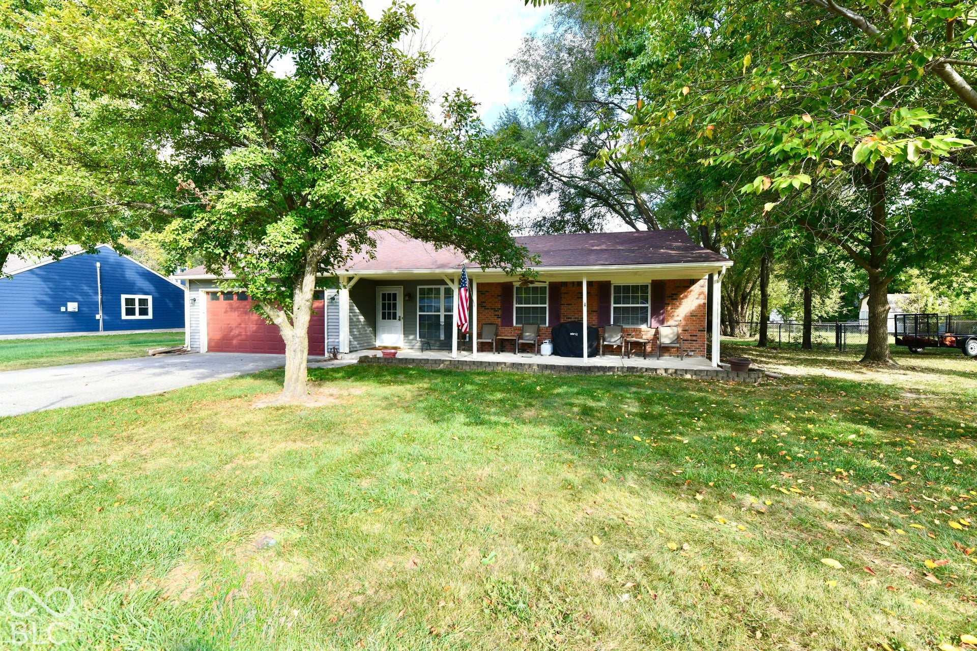Single-story residence featuring a brick and siding exterior, covered front porch, attached garage, and mature trees situated on a lawn