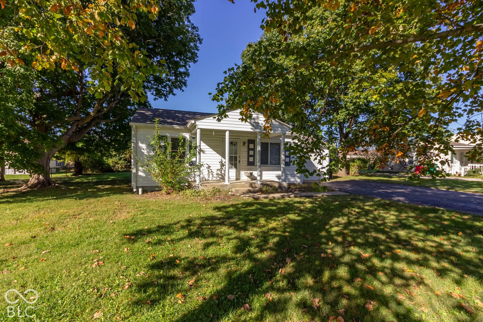 Single-story residence with white siding, covered front porch, asphalt driveway, and mature trees on a level lot