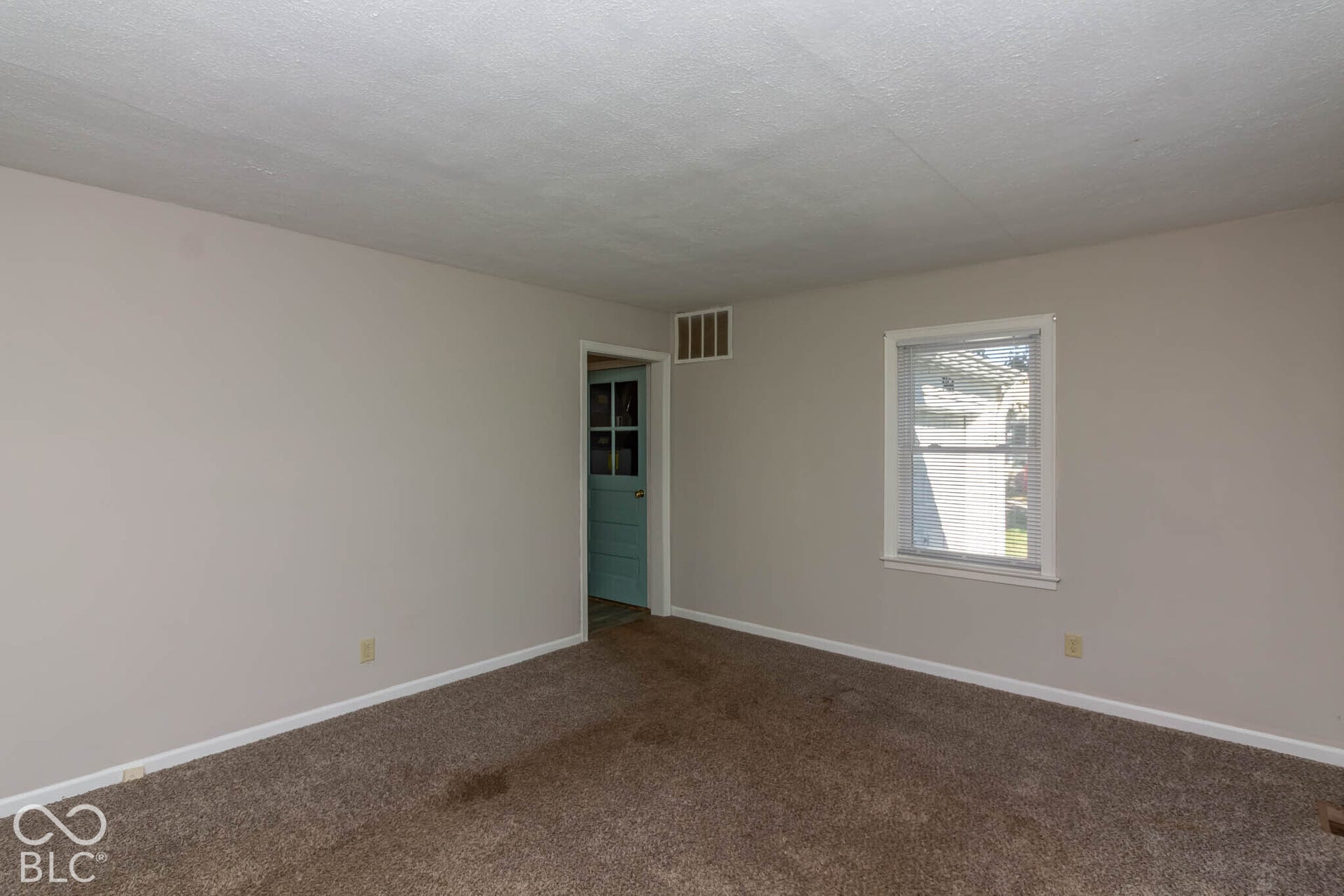 Neutral-toned wall interior featuring carpeting, a single window with white trim, and a doorway with a light blue door