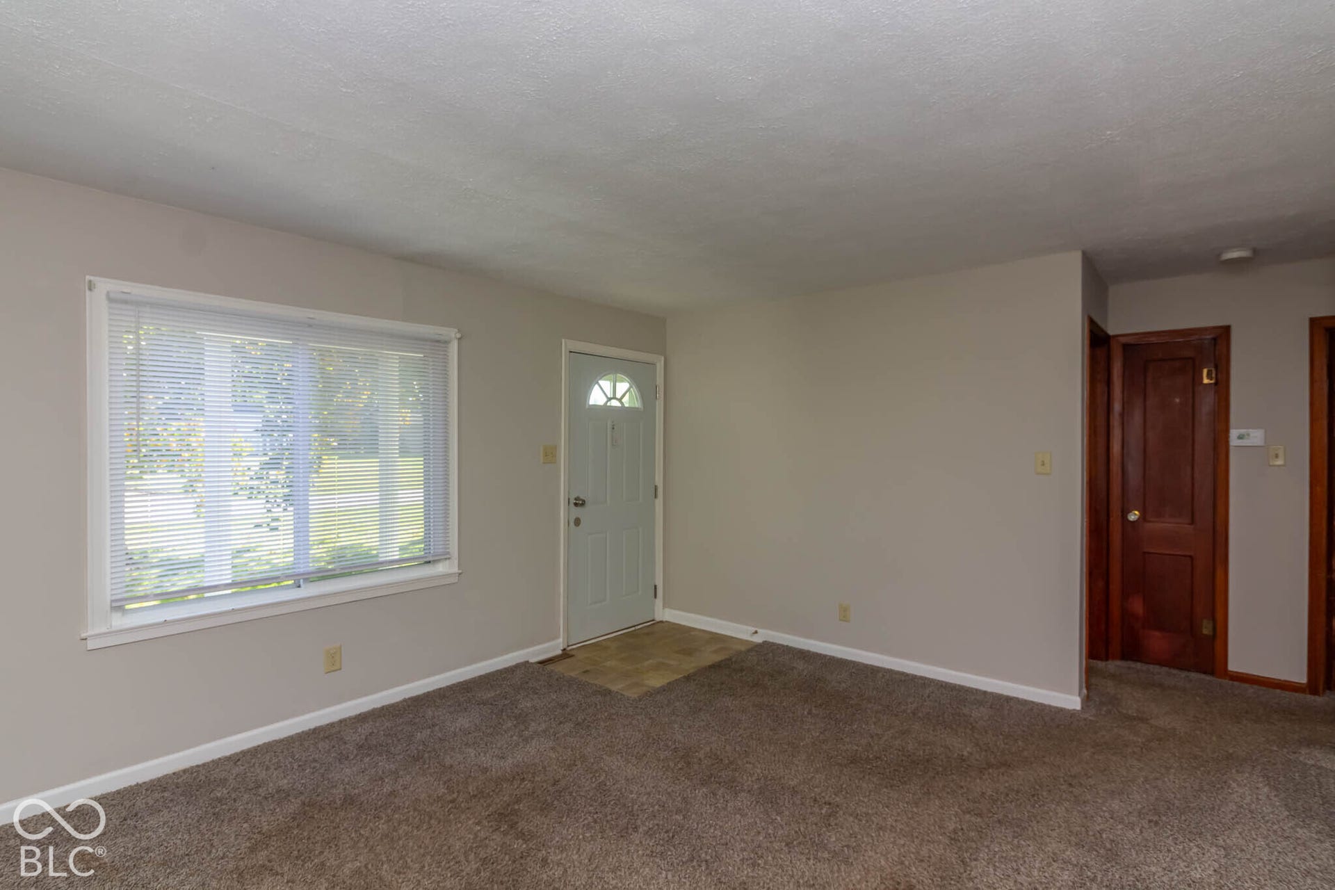 Neutral wall paint, large picture window with blinds, solid wood-finish doors, and tiled entryway flooring