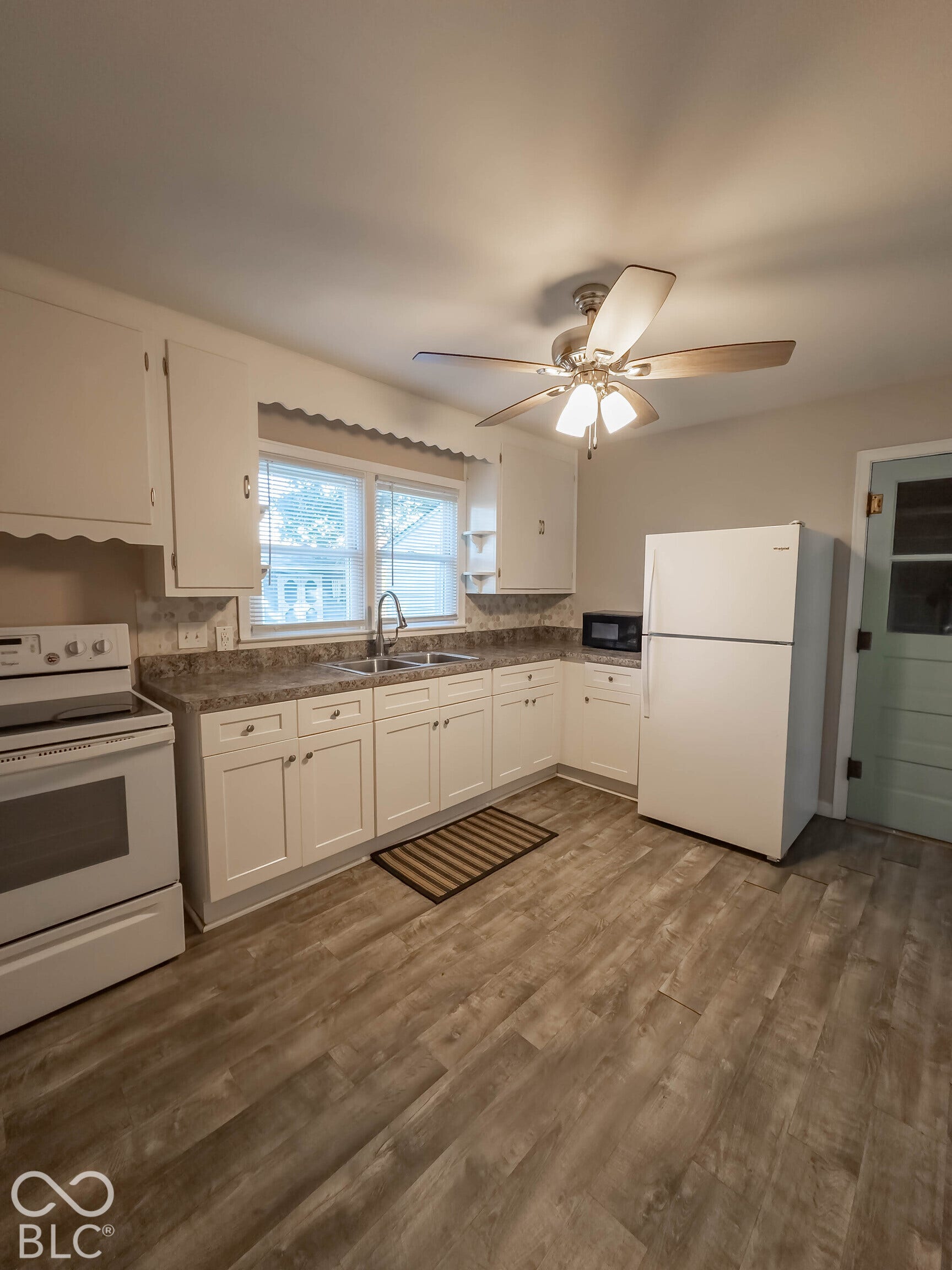 Kitchen featuring white cabinetry, wood-finish flooring, stone-patterned countertops, a dual-basin stainless steel sink, and a ceiling-mounted light fixture with fan