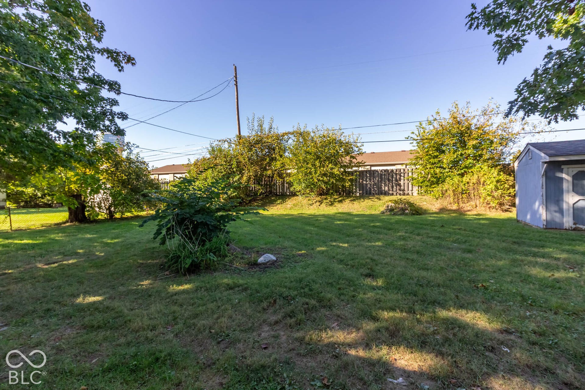 Expansive lawn, mature trees, wood privacy fencing, and detached storage shed