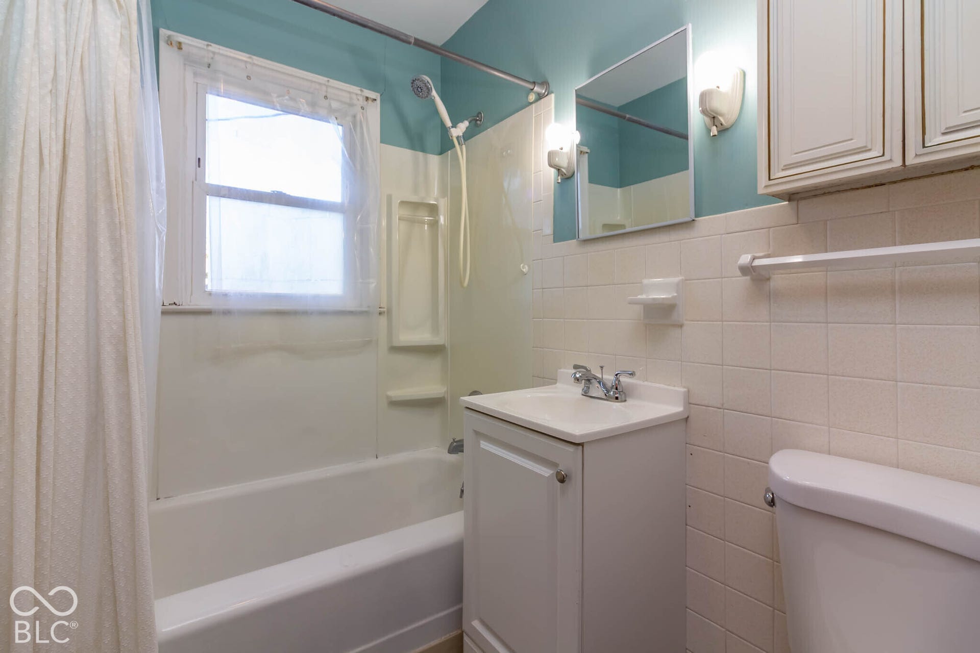 Bathroom featuring a white vanity with an integrated sink, wall-mounted cabinet storage, square wall tiling, and a bathtub with a shower head fixture