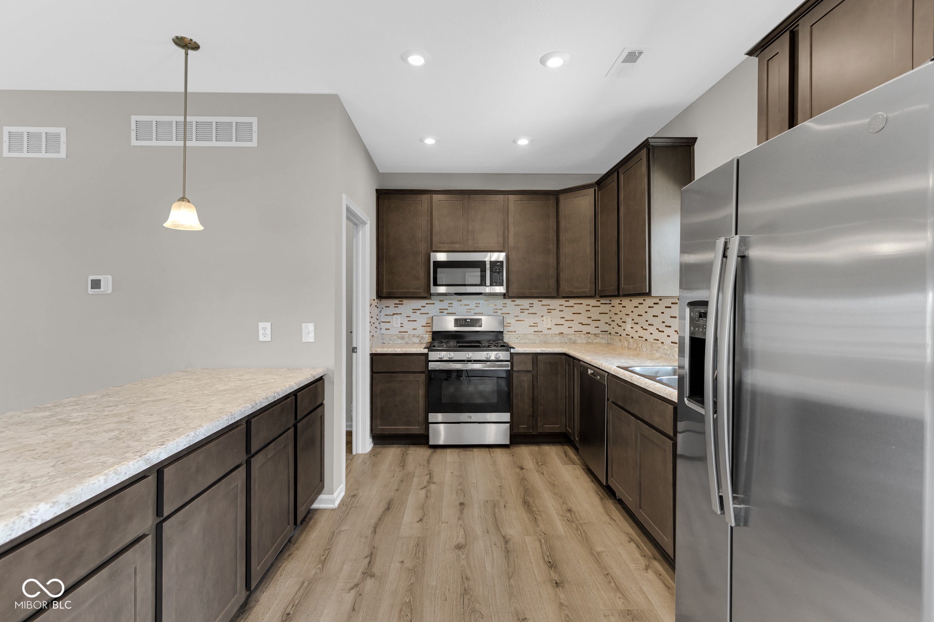 kitchen featuring appliances with stainless steel finishes, light wood-style flooring, dark brown cabinetry, backsplash, and light countertops