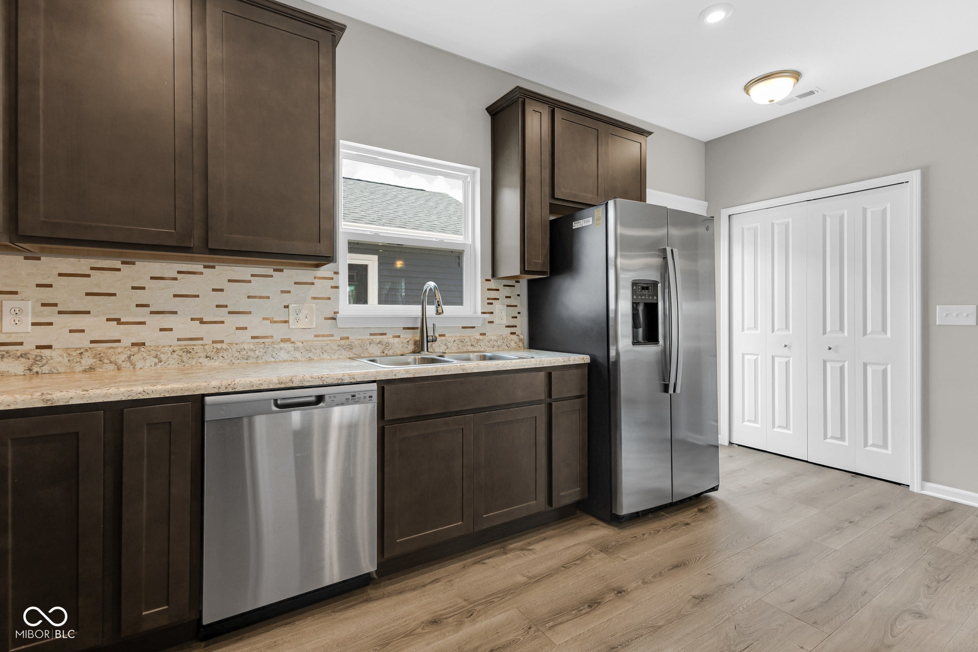 kitchen featuring dark brown cabinets, stainless steel appliances, backsplash, and light wood-style floors