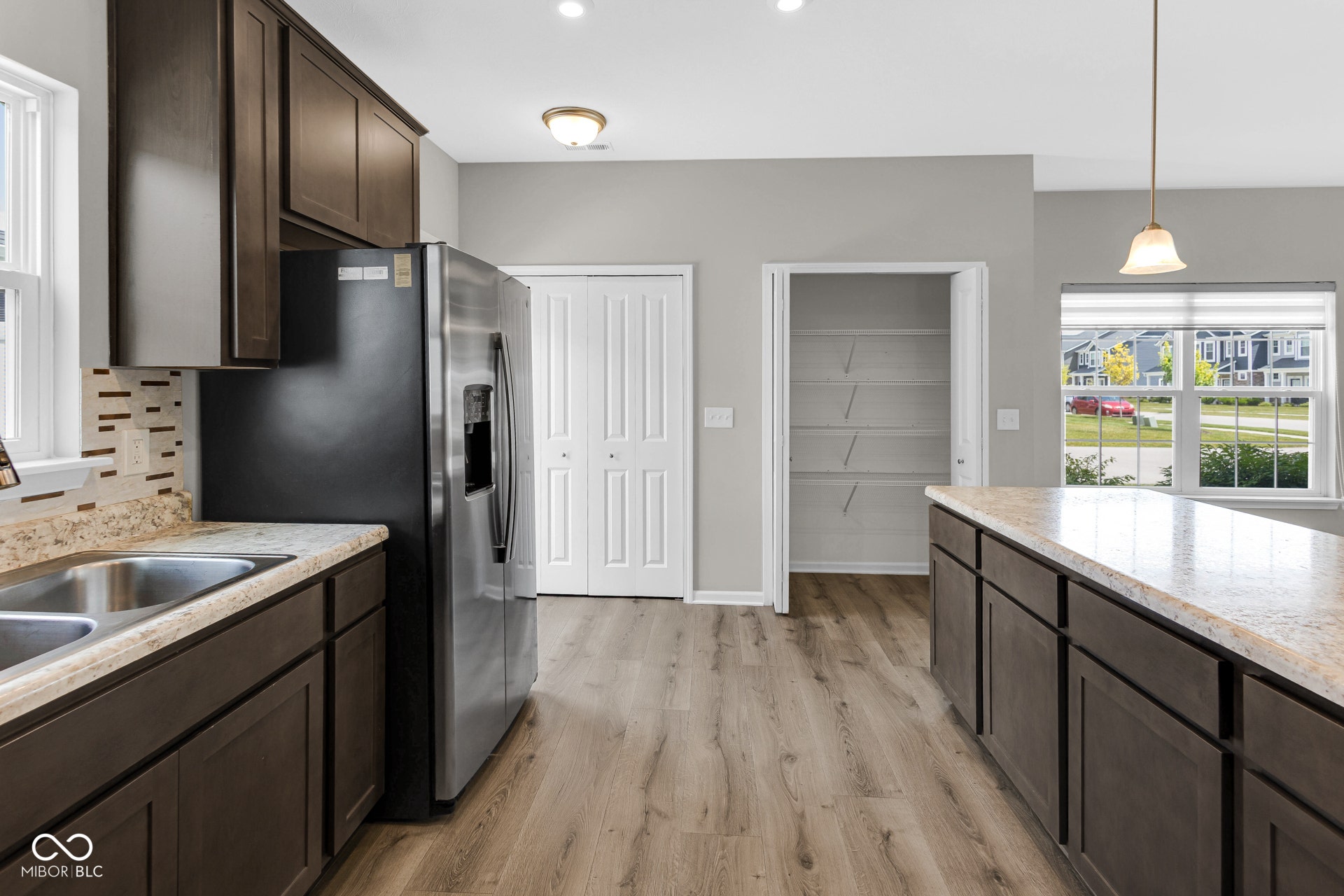 kitchen with dark brown cabinetry, light wood-style floors, stainless steel fridge with ice dispenser, pendant lighting, and backsplash