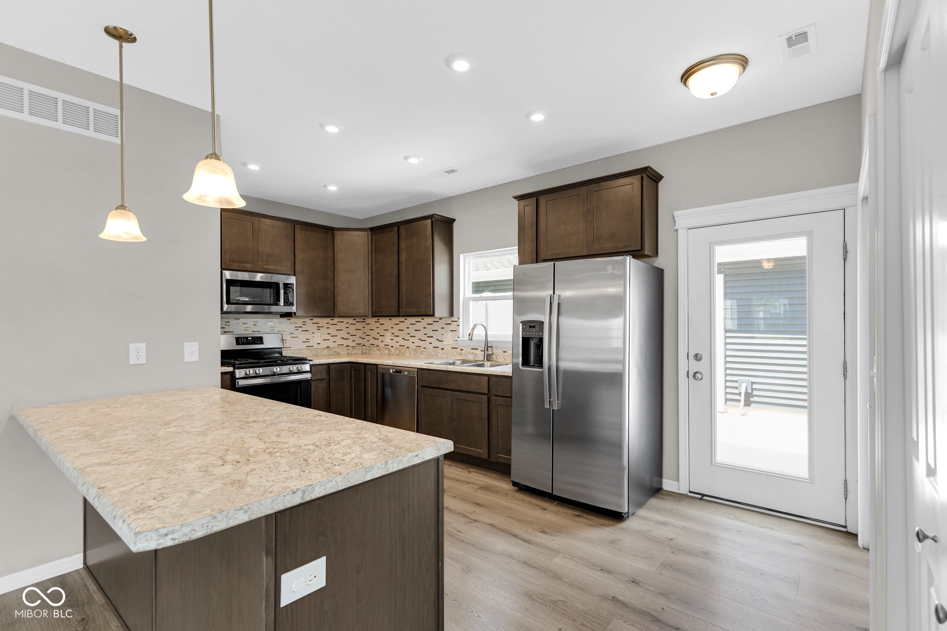 kitchen with appliances with stainless steel finishes, dark brown cabinetry, light countertops, decorative backsplash, and light wood-type flooring