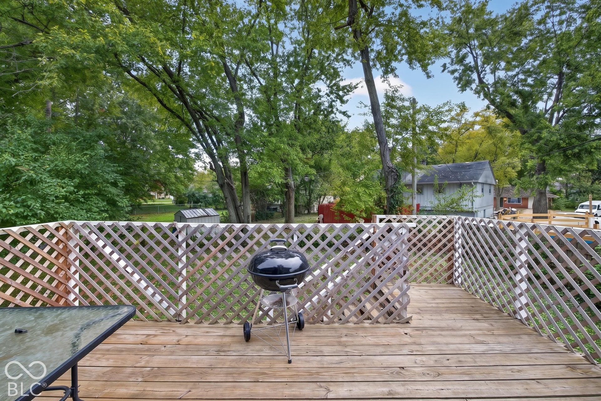 Spacious composite deck with lattice privacy fencing, mature tree canopy, and charcoal grill-ideal for outdoor entertaining and relaxation