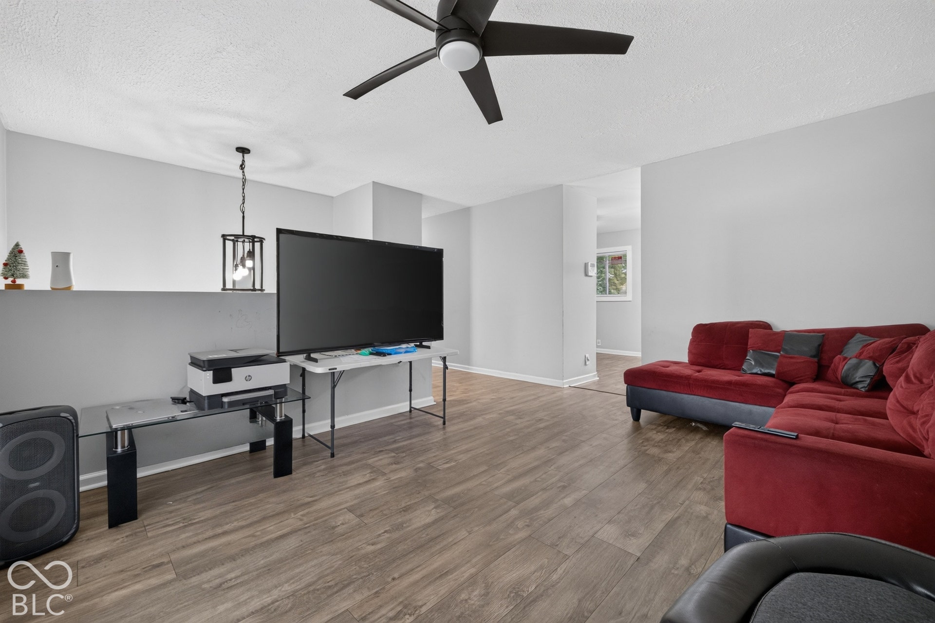Neutral interior space featuring wood-finish flooring, a ceiling fan with integrated lighting, and a hanging pendant fixture
