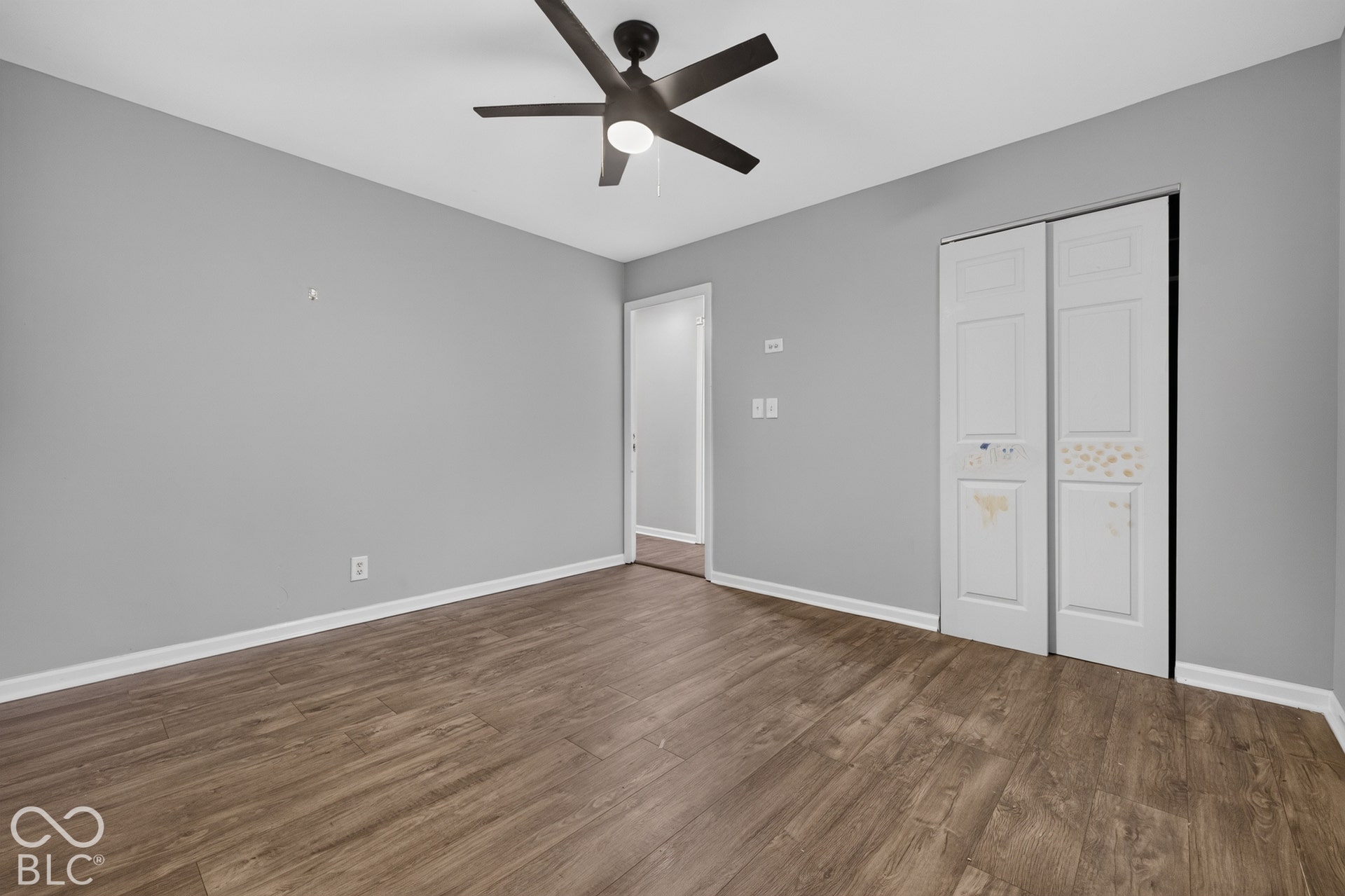 Room featuring wood-finish flooring, a neutral-toned wall finish, and a ceiling-mounted fan with integrated lighting