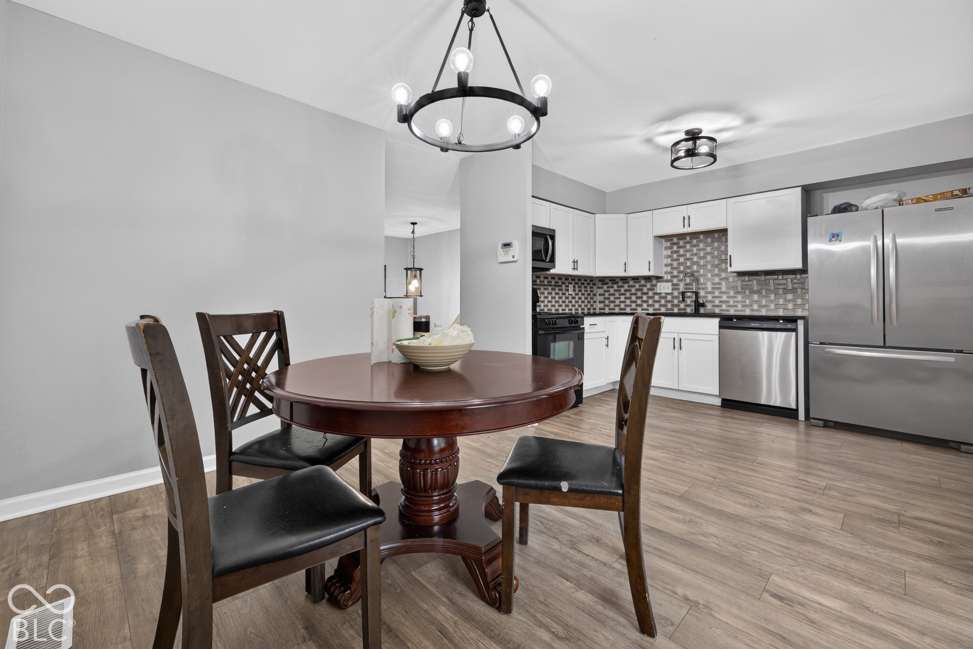 Kitchen featuring white shaker-style cabinetry, stainless steel appliances, patterned tile backsplash, wood-finish flooring, and a modern wagon-wheel chandelier