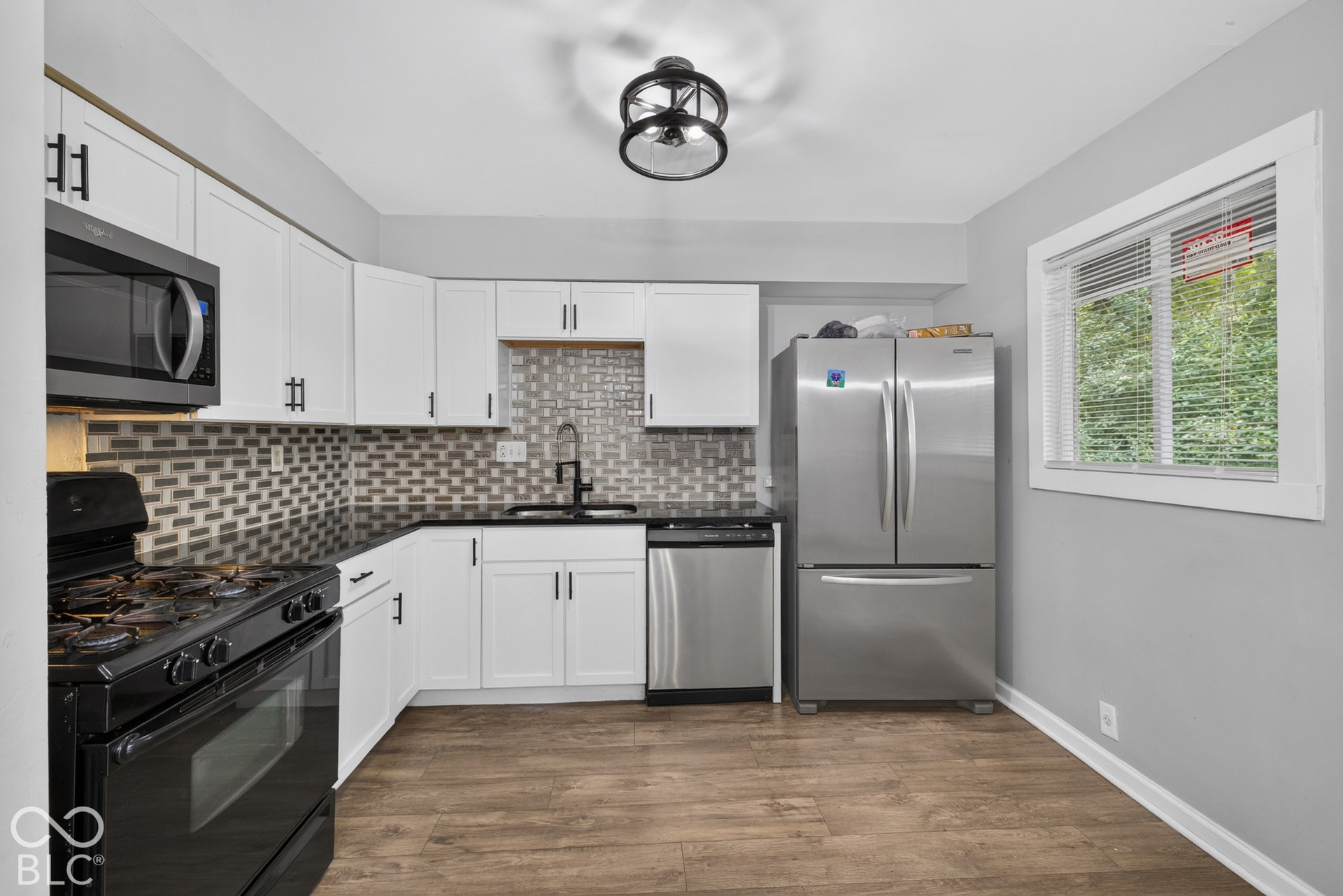 Kitchen featuring white cabinetry, dark countertops, a multi-tonal backsplash, stainless steel appliances, and wood-finish flooring