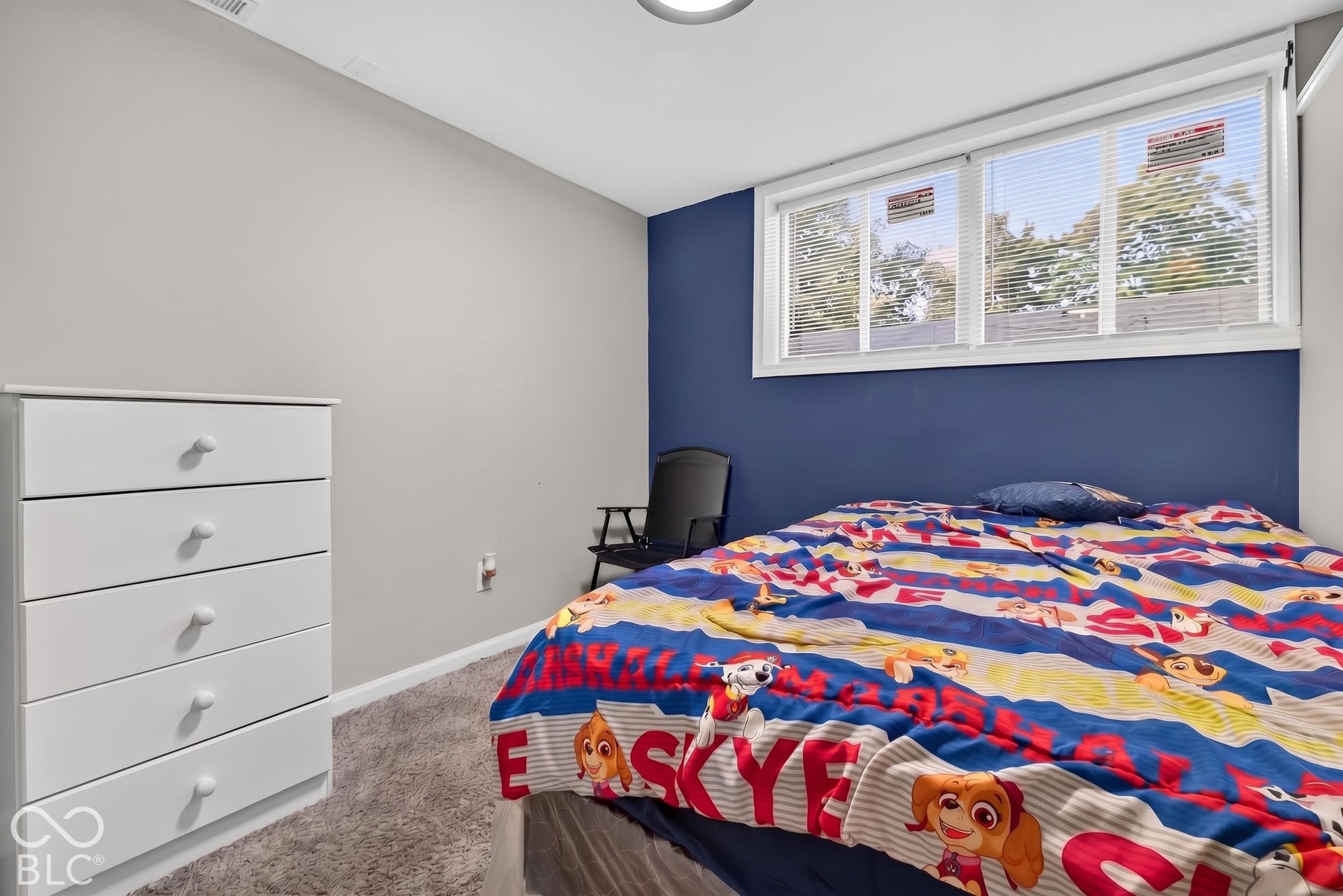 Room interior featuring neutral wall paint, a bold blue accent wall, carpeted flooring, and a multi-pane horizontal window