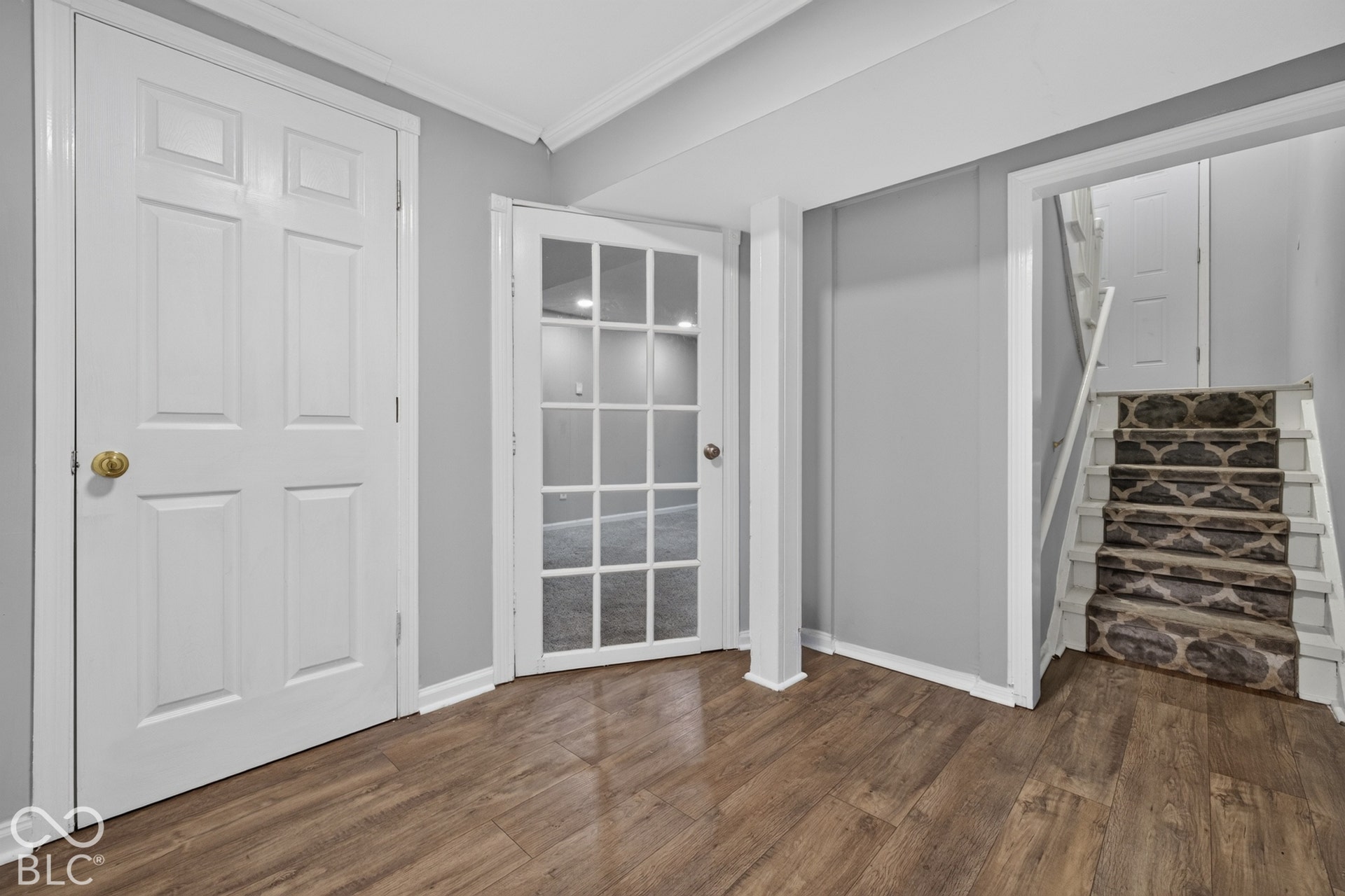 Interior space featuring wood-finish flooring, a glass-panel French door, a solid-panel door with brass hardware, and a staircase with patterned carpeting
