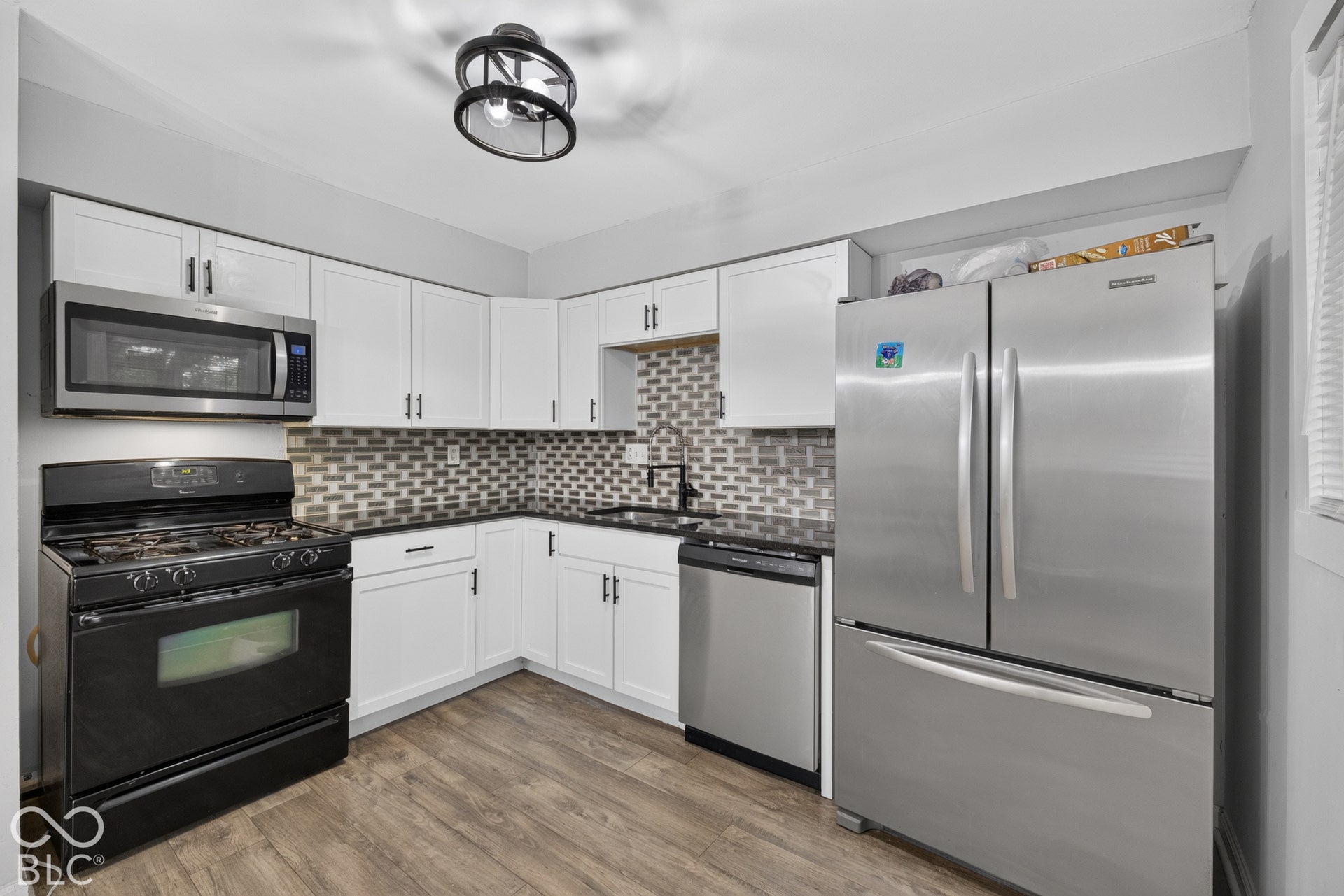 Kitchen featuring white cabinetry, wood-finish flooring, brick-pattern backsplash, stainless steel appliances, and a matte black gooseneck faucet