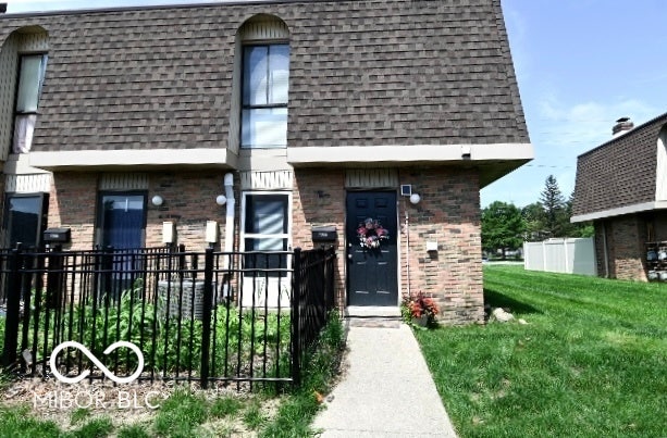 Brick exterior featuring a dark entry door with exterior lighting, an architectural shingle roof, a concrete walkway, and a fenced front patio area