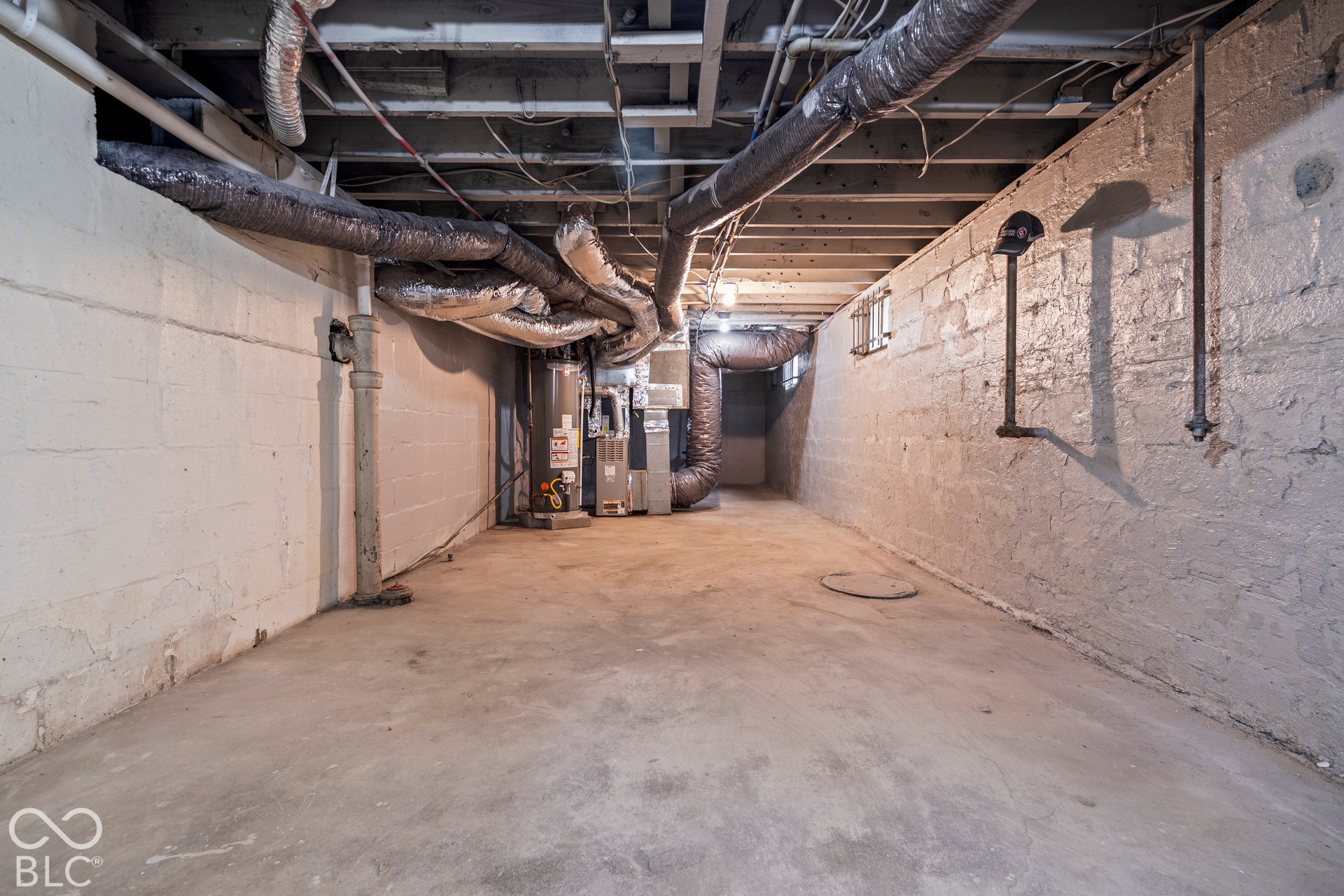 Unfinished basement area featuring exposed ceiling joists, painted concrete block walls, concrete flooring, and an installed water heater and furnace system