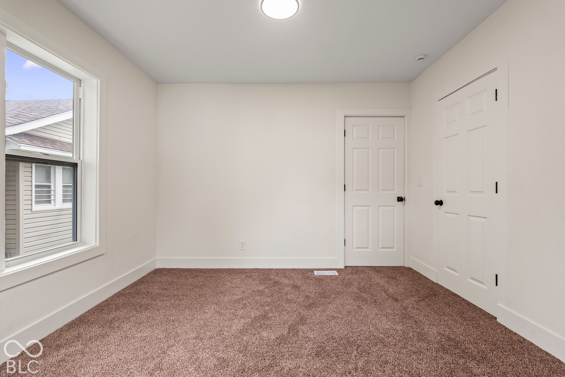 Interior space featuring neutral-toned carpeting, high-gloss white paneled doors with matte black hardware, and a single-pane window with white trim