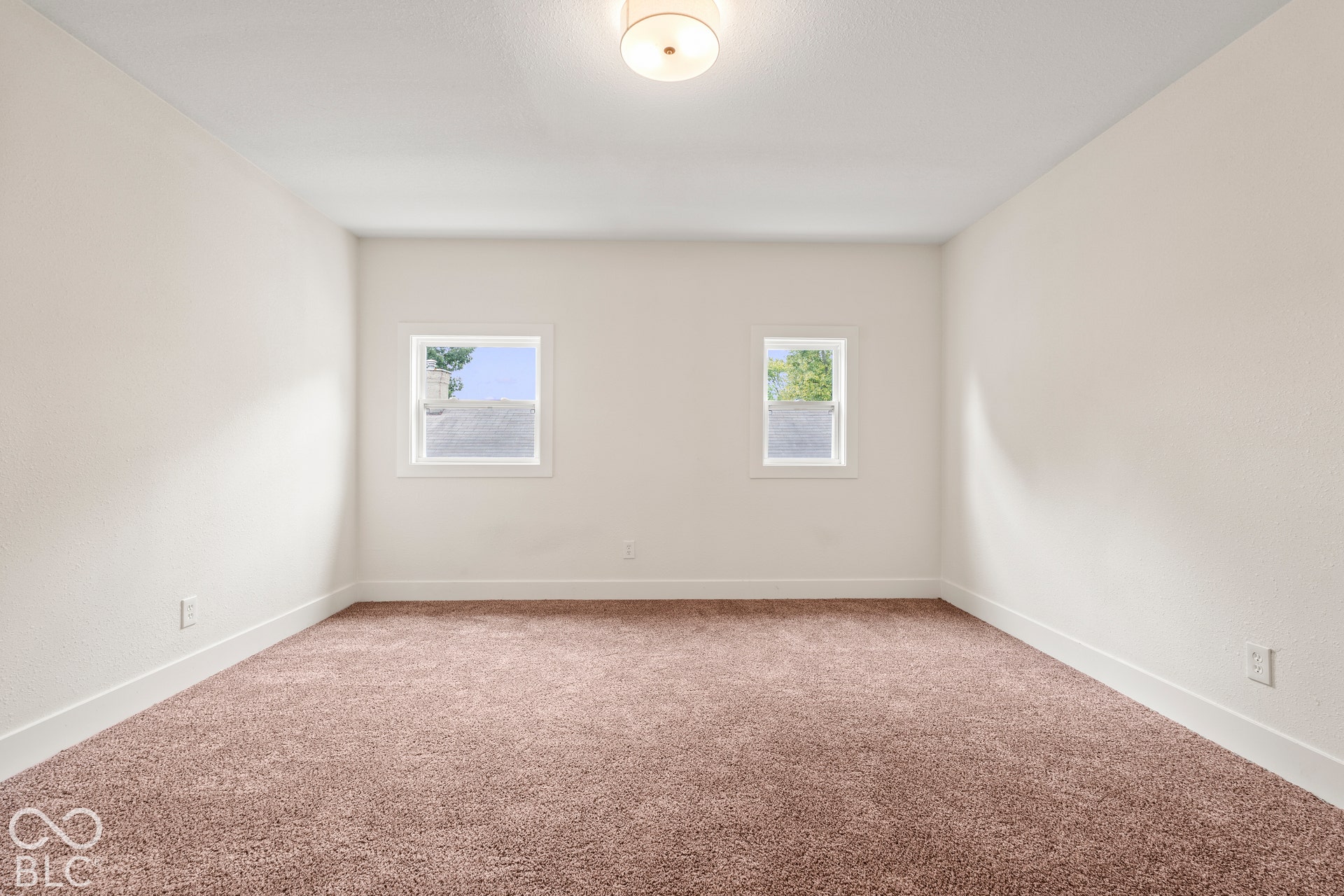 Neutral-toned interior space featuring wall-to-wall carpeting, dual windows with white casing, and a centered flush-mount light fixture