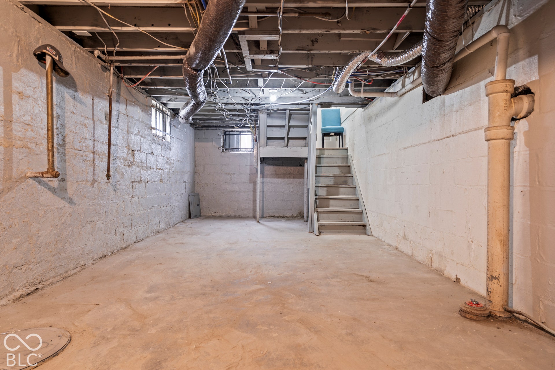 Unfinished lower level with concrete flooring, painted masonry walls, exposed ceiling joists, and small operational windows