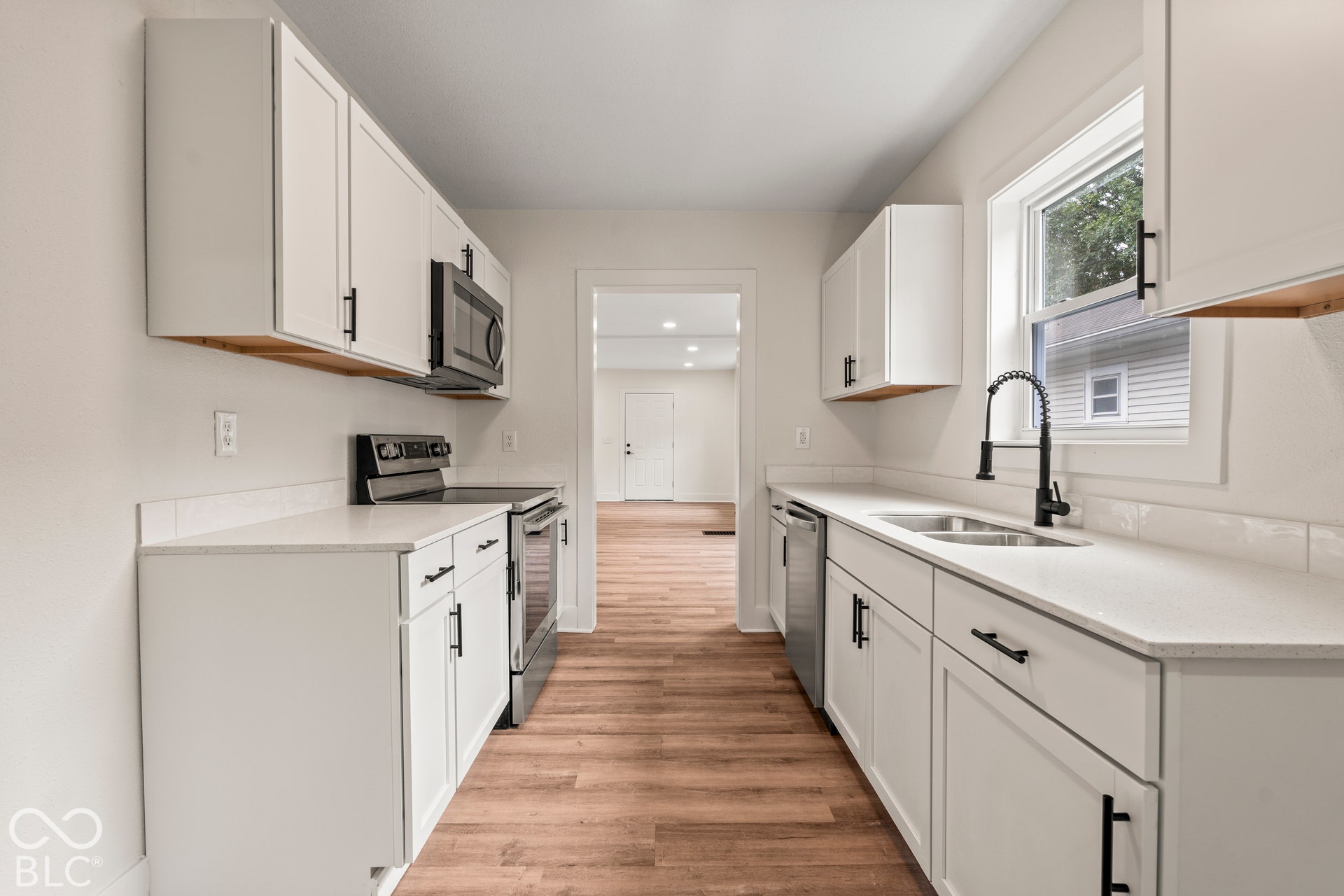 Kitchen featuring white shaker-style cabinetry, solid-surface countertops, wood-finish flooring, stainless steel appliances, and a matte black gooseneck faucet