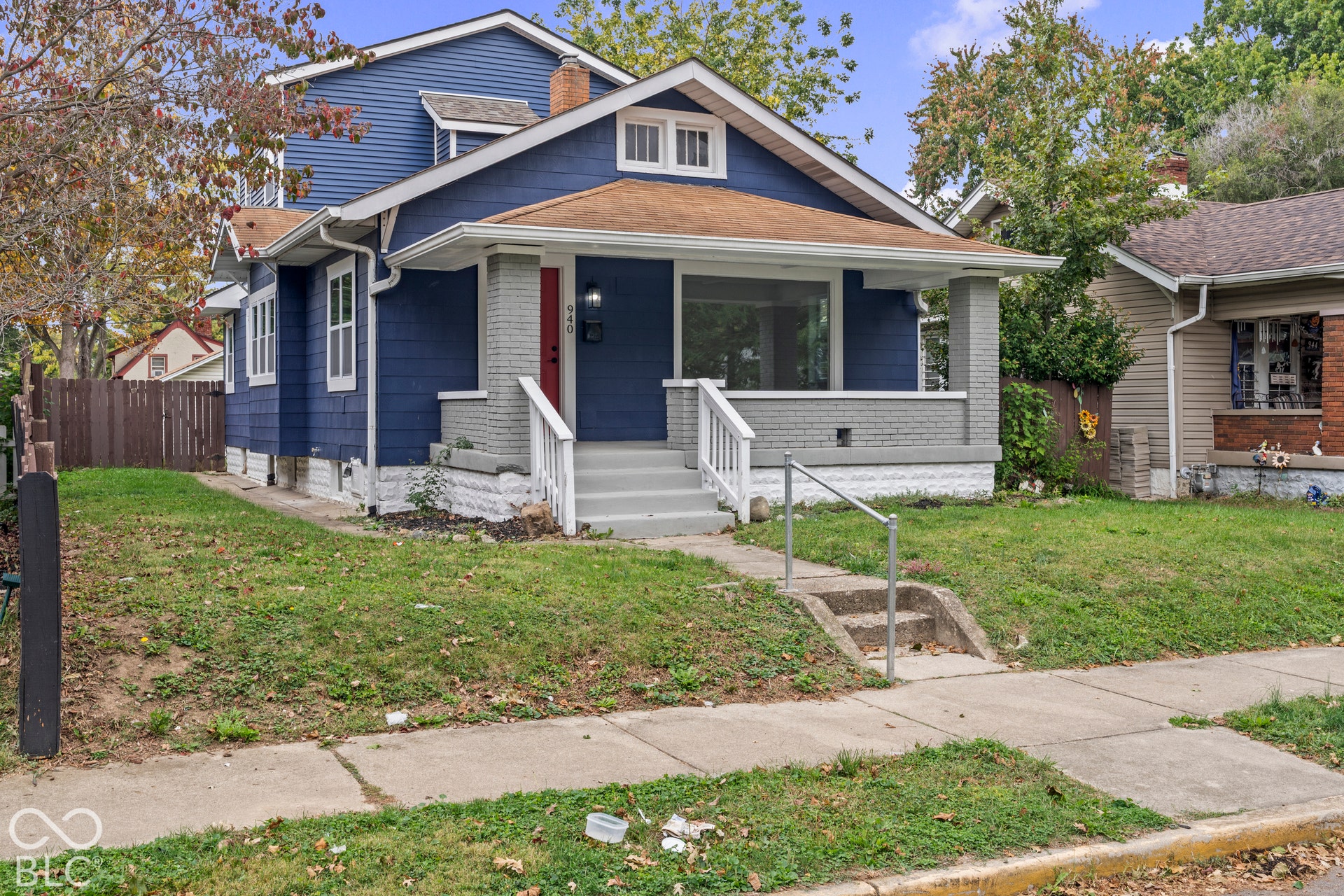 Craftsman-style exterior featuring blue shake siding, a covered front porch with masonry pillars, a gabled roofline, and a concrete walkway