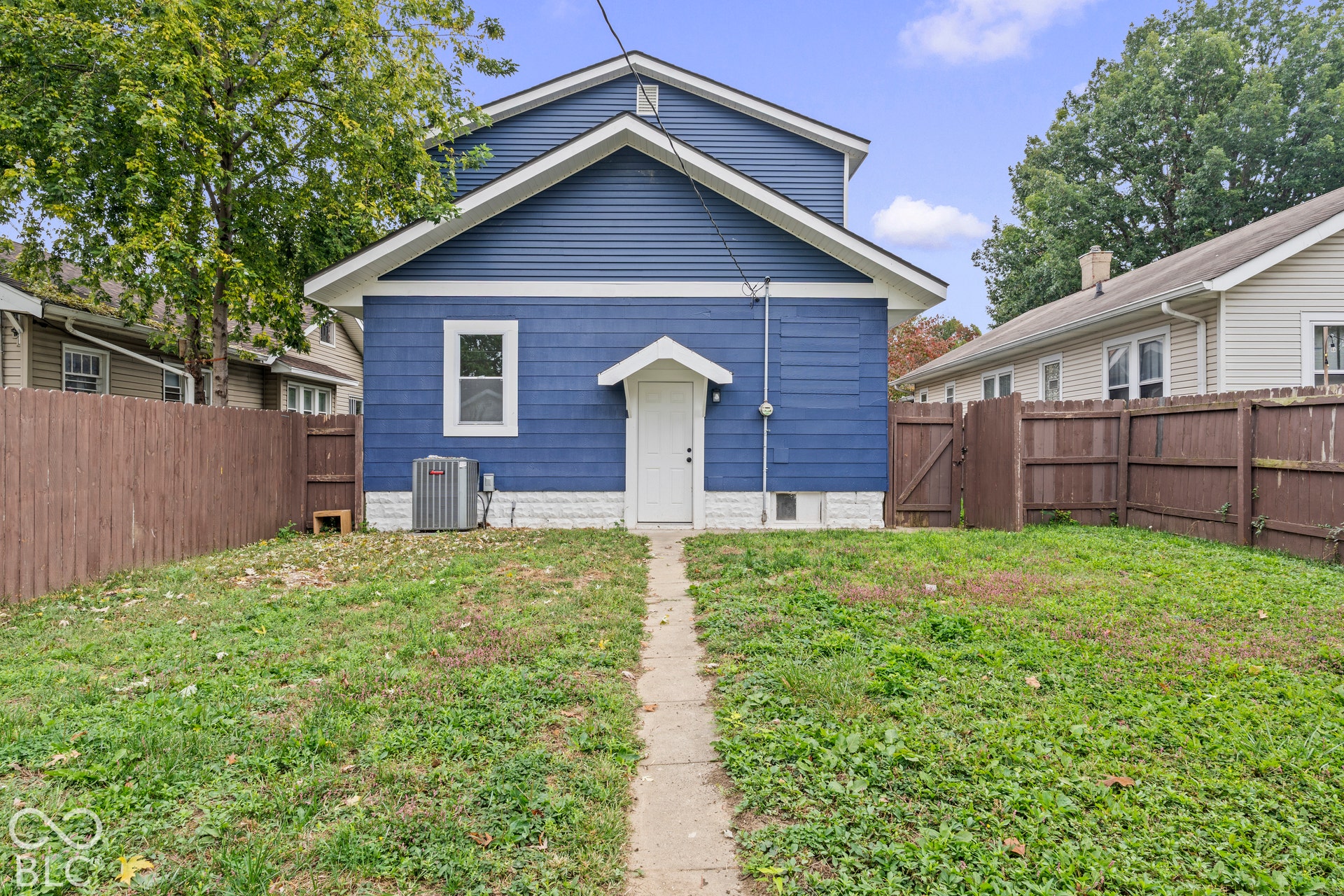 Exterior rear view featuring blue horizontal siding, white trim accents, a concrete walkway, and wood perimeter fencing