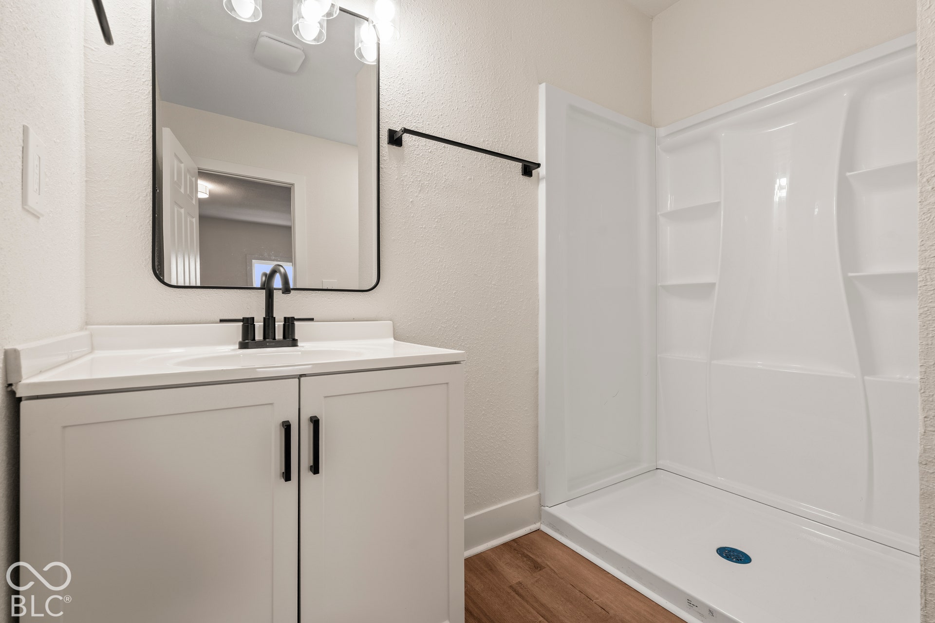 Bathroom featuring a vanity with white cabinetry, a rectangular mirror with a rounded black frame, a matte black faucet, and a white walk-in shower surround