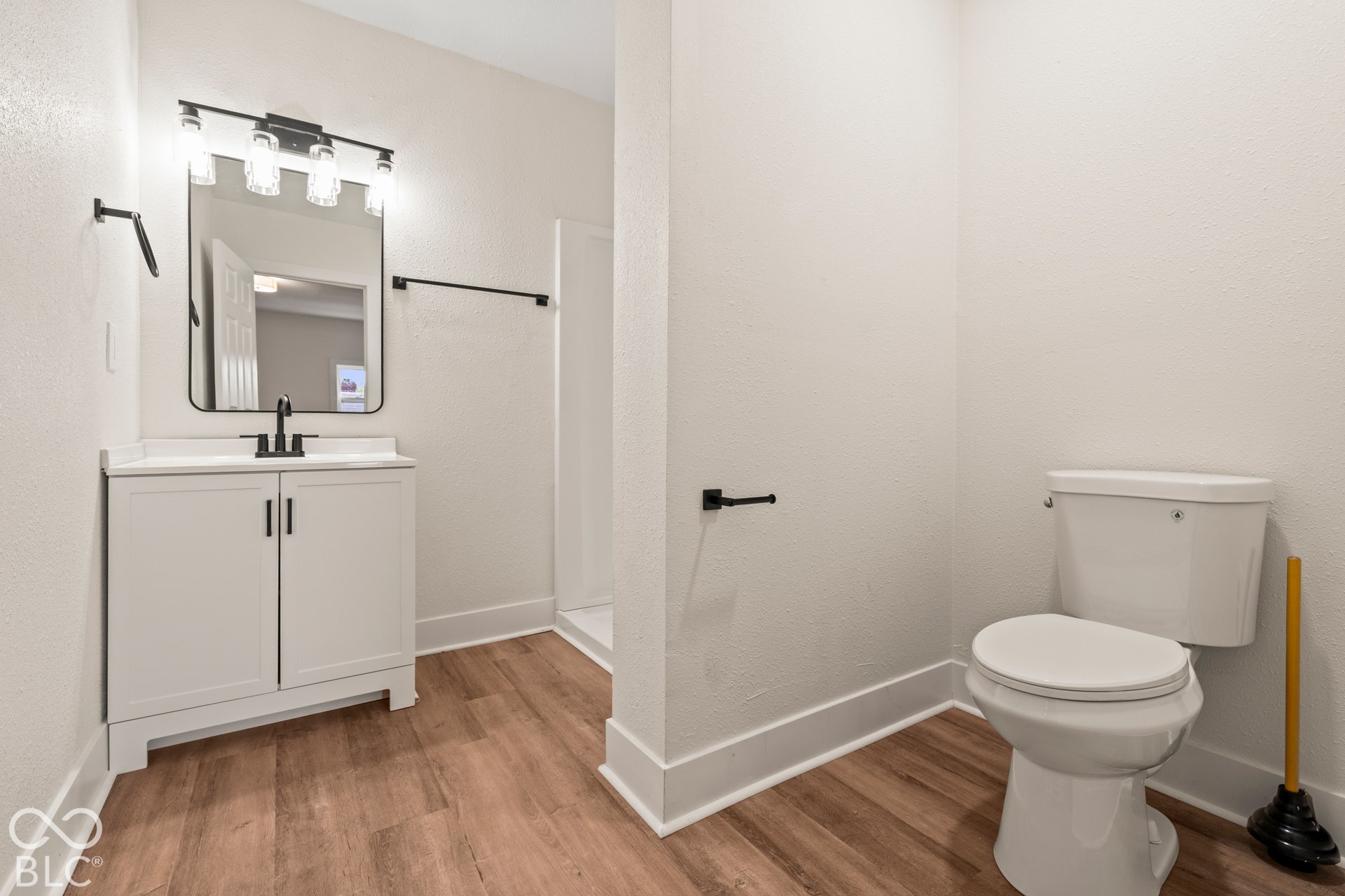 Bathroom featuring a white vanity cabinet, rectangular mirror, wood-finish flooring, four-light vanity fixture, and matte black hardware