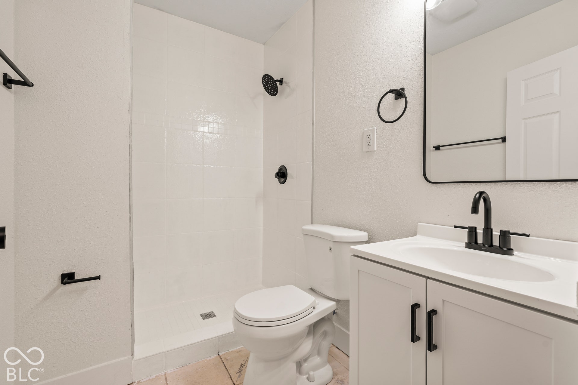 Bathroom featuring a white vanity cabinet with matte black hardware, a rectangular sink with a matte black faucet, a walk-in shower with matte black fixtures, and a rectangular mirror with a black frame