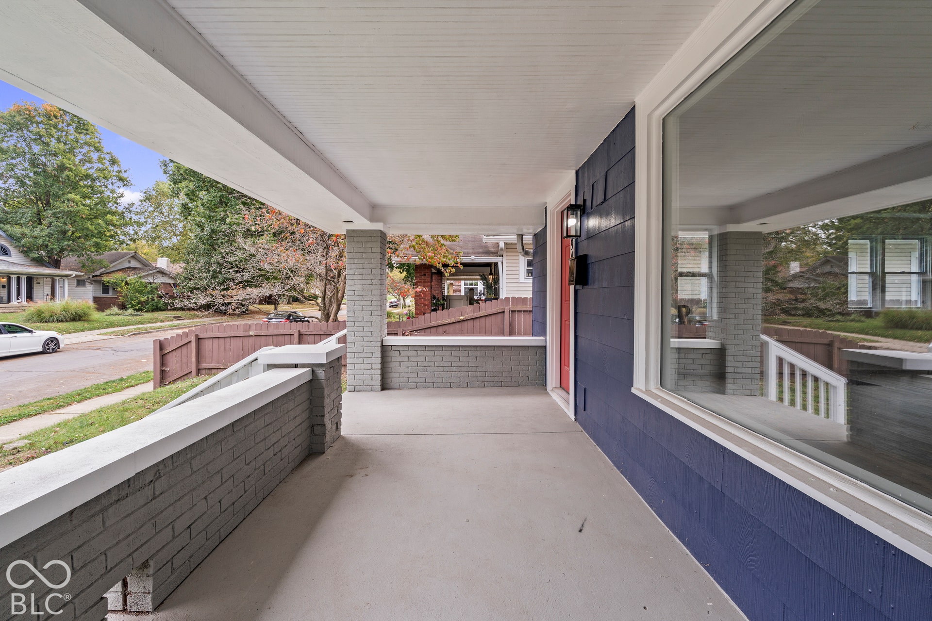 Covered porch featuring painted brick half-walls, concrete flooring, shake-style exterior siding, and a large picture window