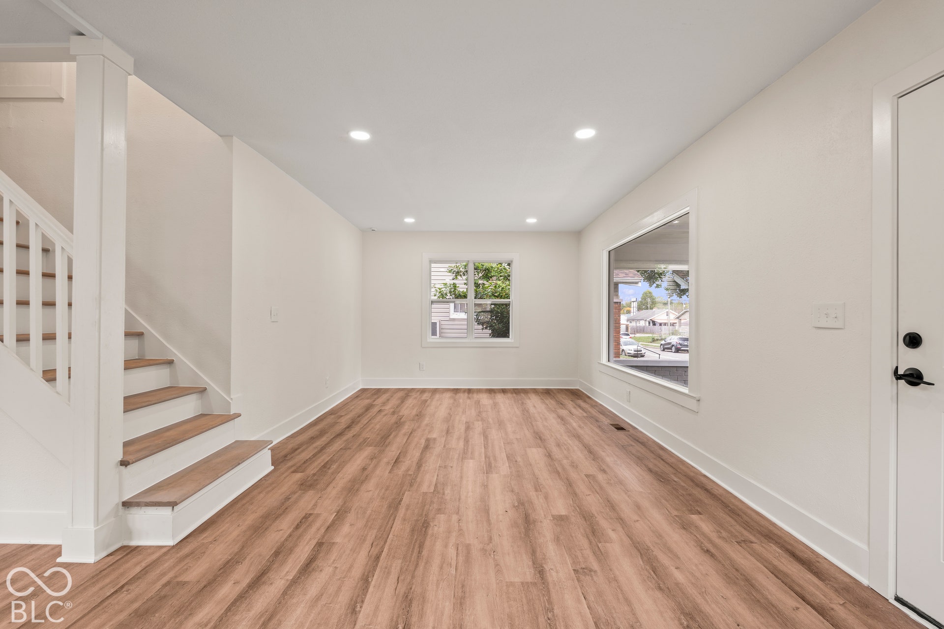 Neutral interior space featuring wood-finish flooring, recessed lighting, large picture windows, and a staircase with a white railing