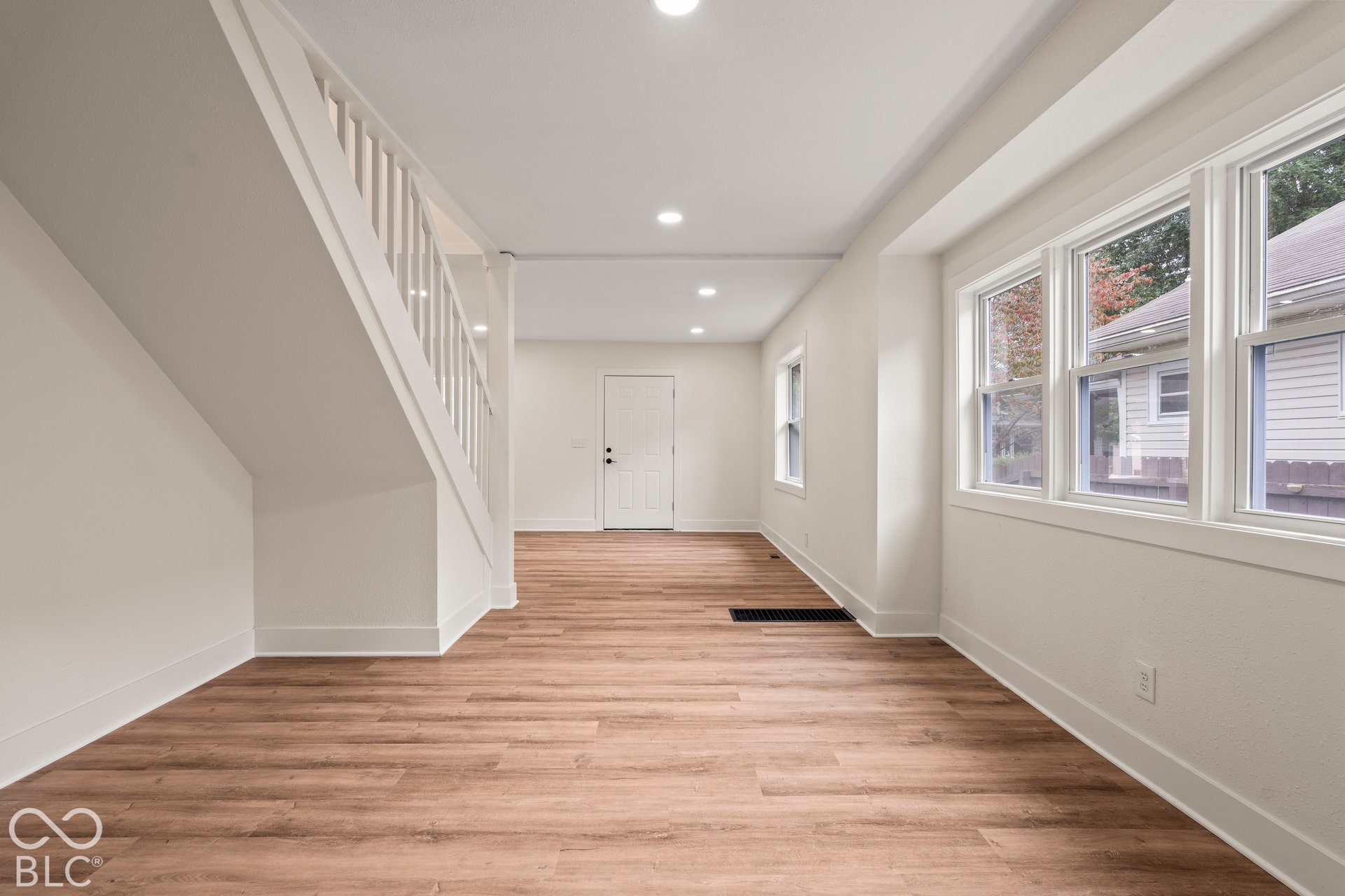 Neutral interior featuring wood-finish flooring, recessed lighting, white staircase railing, and large multi-pane windows