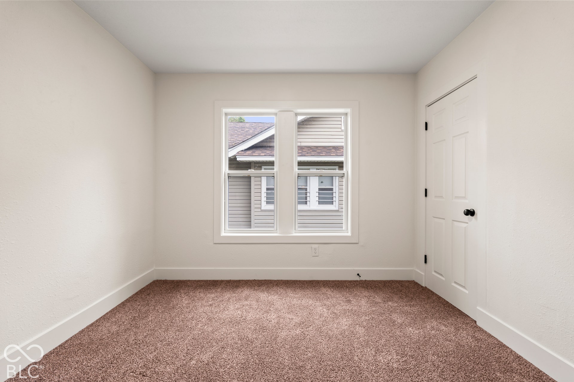 Neutral-toned room featuring neutral carpeting, a central double-pane window, and a white six-panel interior door with dark hardware