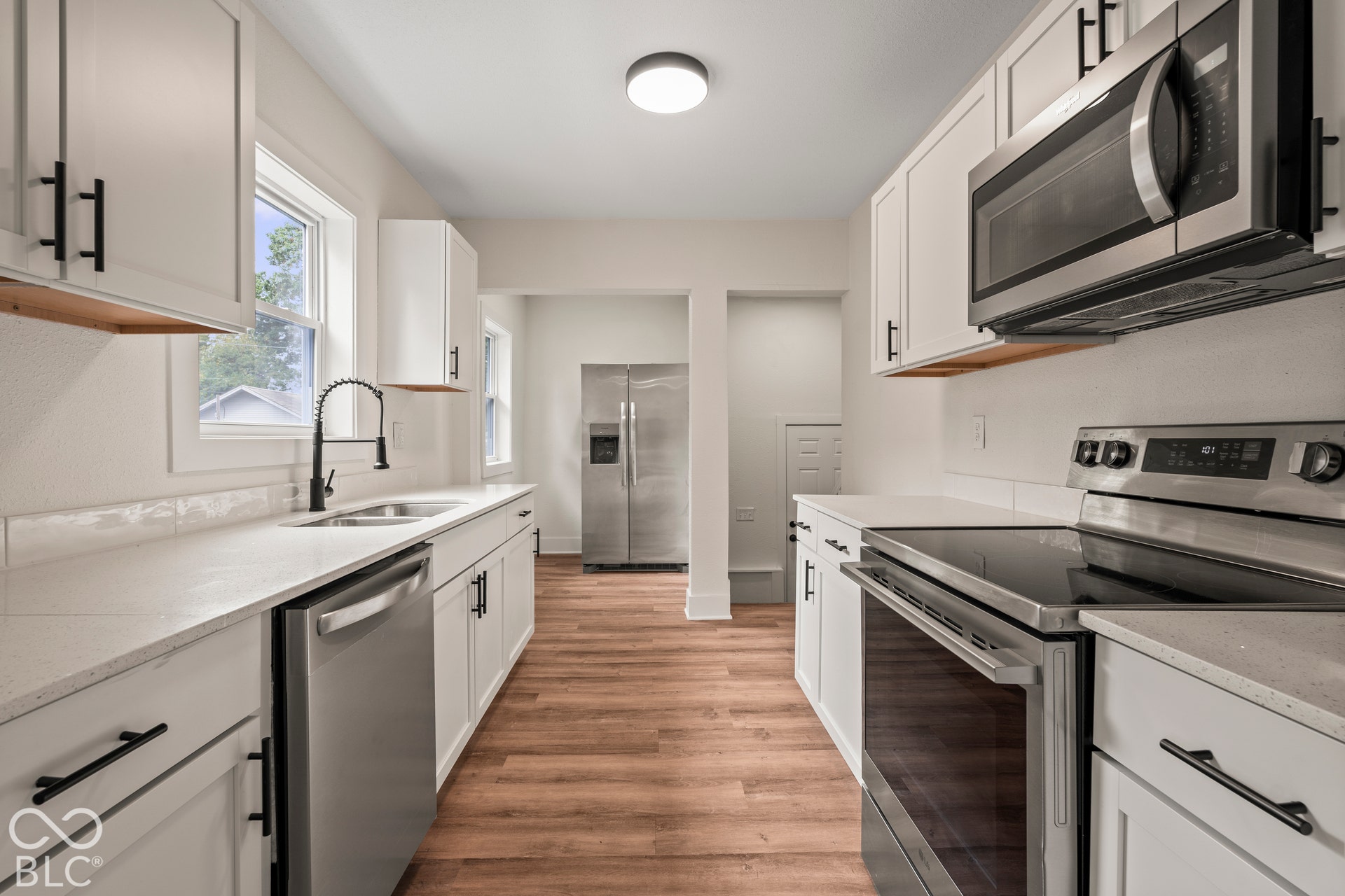 Kitchen featuring white shaker-style cabinetry, quartz countertops, stainless steel appliances, a high-arc pull-down faucet, and wood-finish flooring