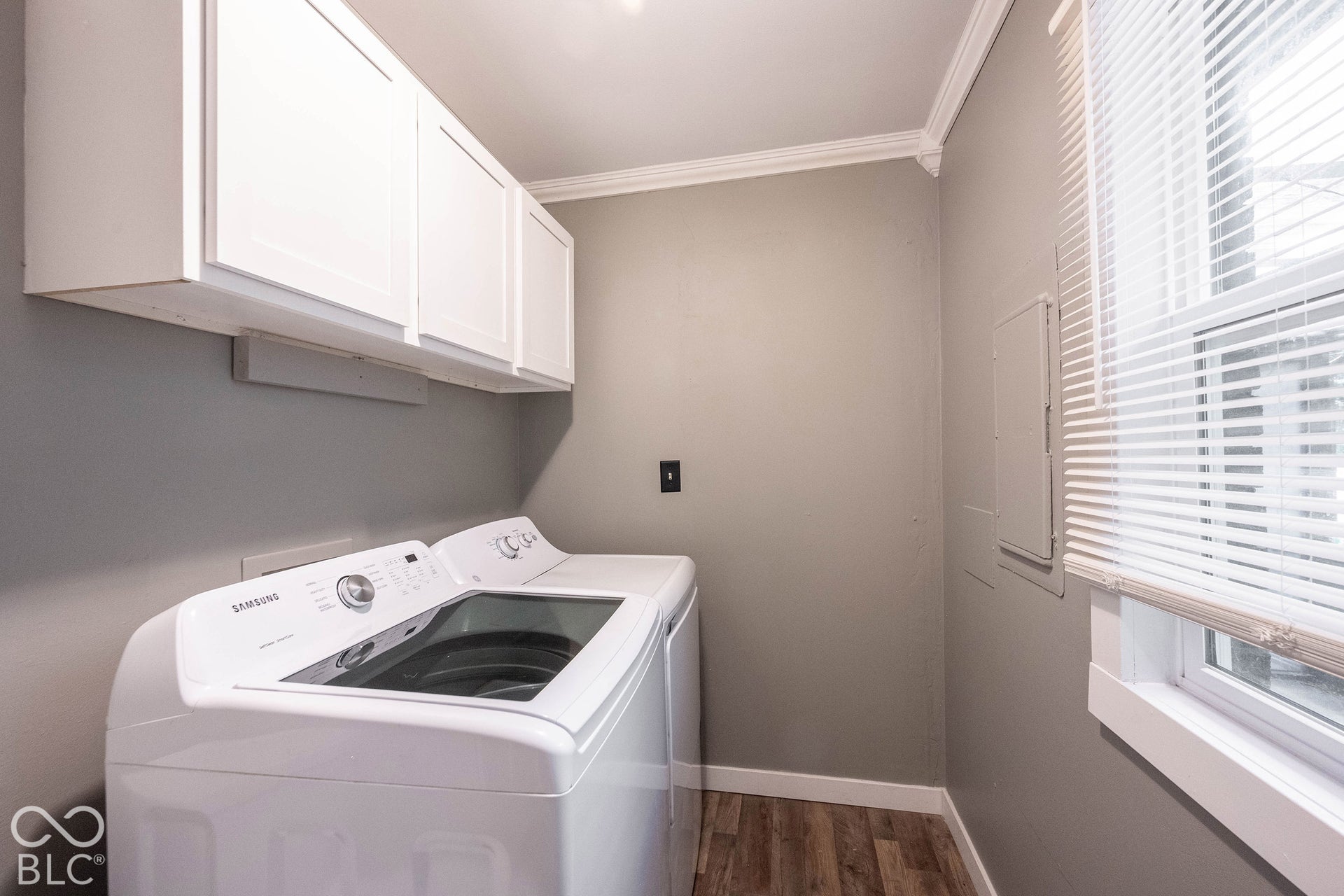 Laundry area featuring upper white cabinetry, wood-finish flooring, and crown molding