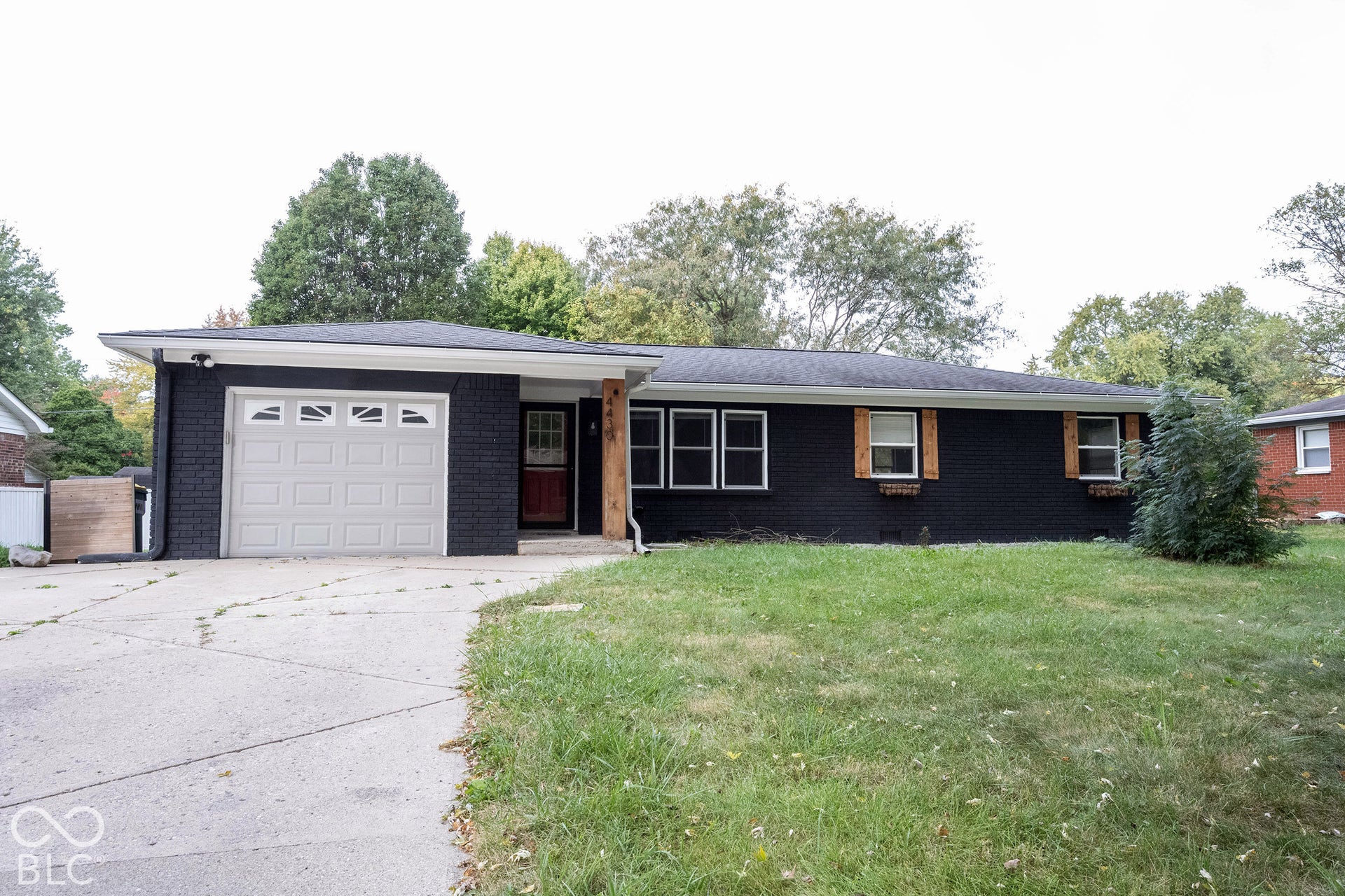 Single-story exterior featuring a dark brick facade, attached one-car garage, wood-textured shutters, and a concrete driveway