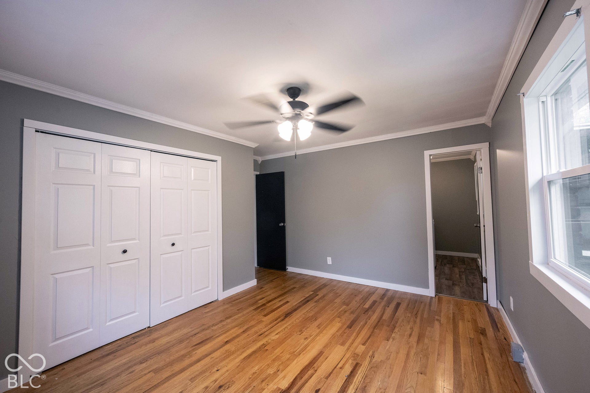 Hardwood flooring, crown molding, multi-panel bifold closet doors, and a ceiling-mounted light fixture with a fan