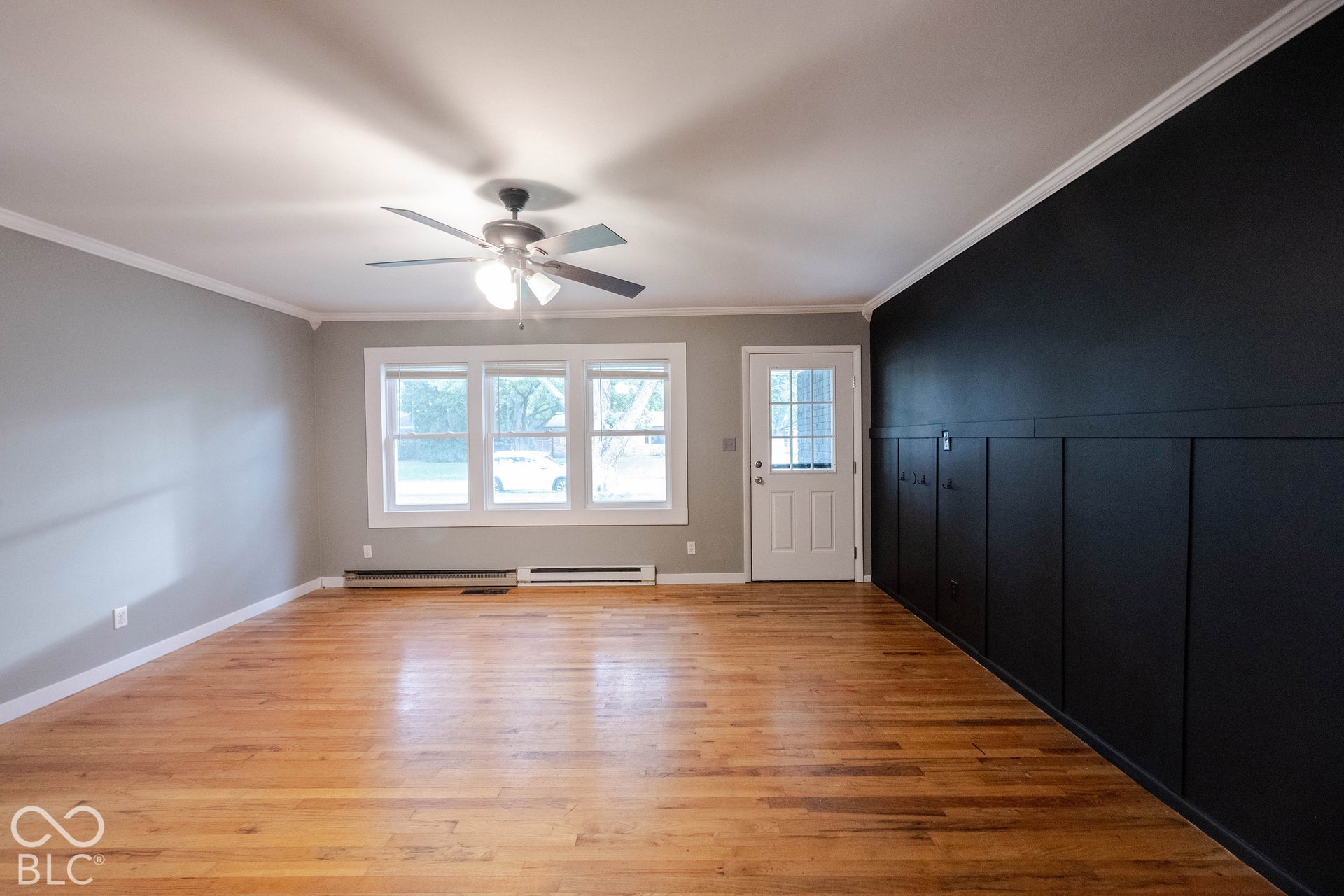 Interior space featuring wood-finish flooring, a matte black board-and-batten accent wall, triple-pane window, and a ceiling-mounted light fixture with fan