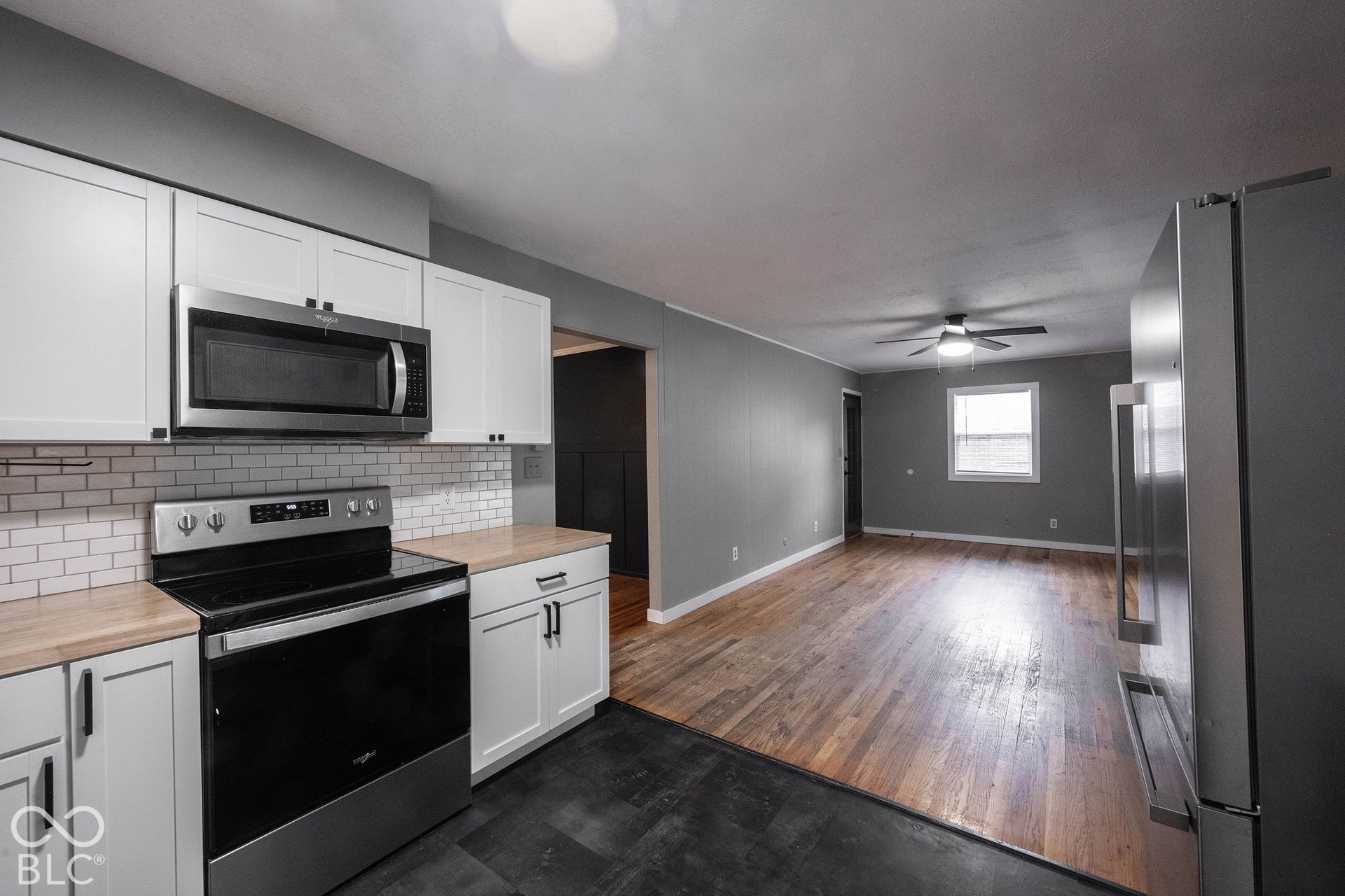 Kitchen featuring white cabinetry, subway tile backsplash, wood-finish countertops, stainless steel appliances, and wood-finish flooring