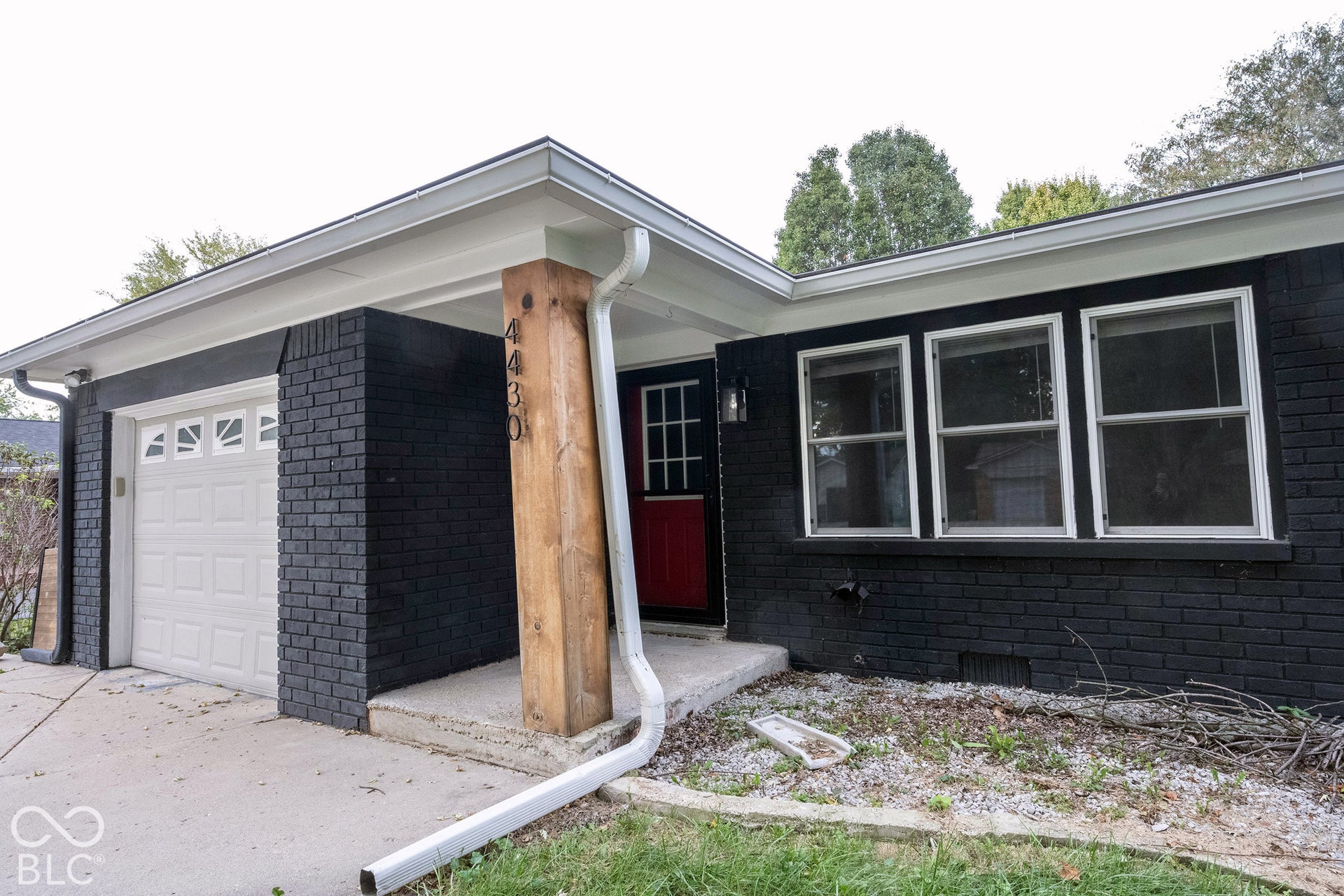 Exterior featuring dark-toned brick masonry, a substantial exposed-timber support post, a single-car garage with a paneled door, and multi-pane front entry door
