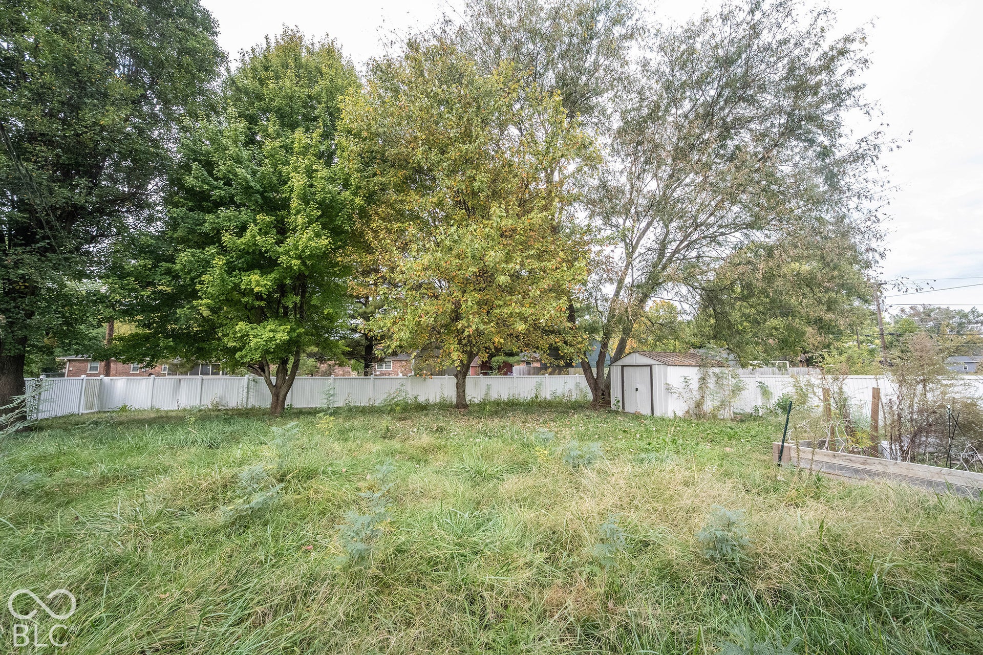 Expansive backyard featuring mature trees, a detached storage shed, and a perimeter vinyl privacy fence