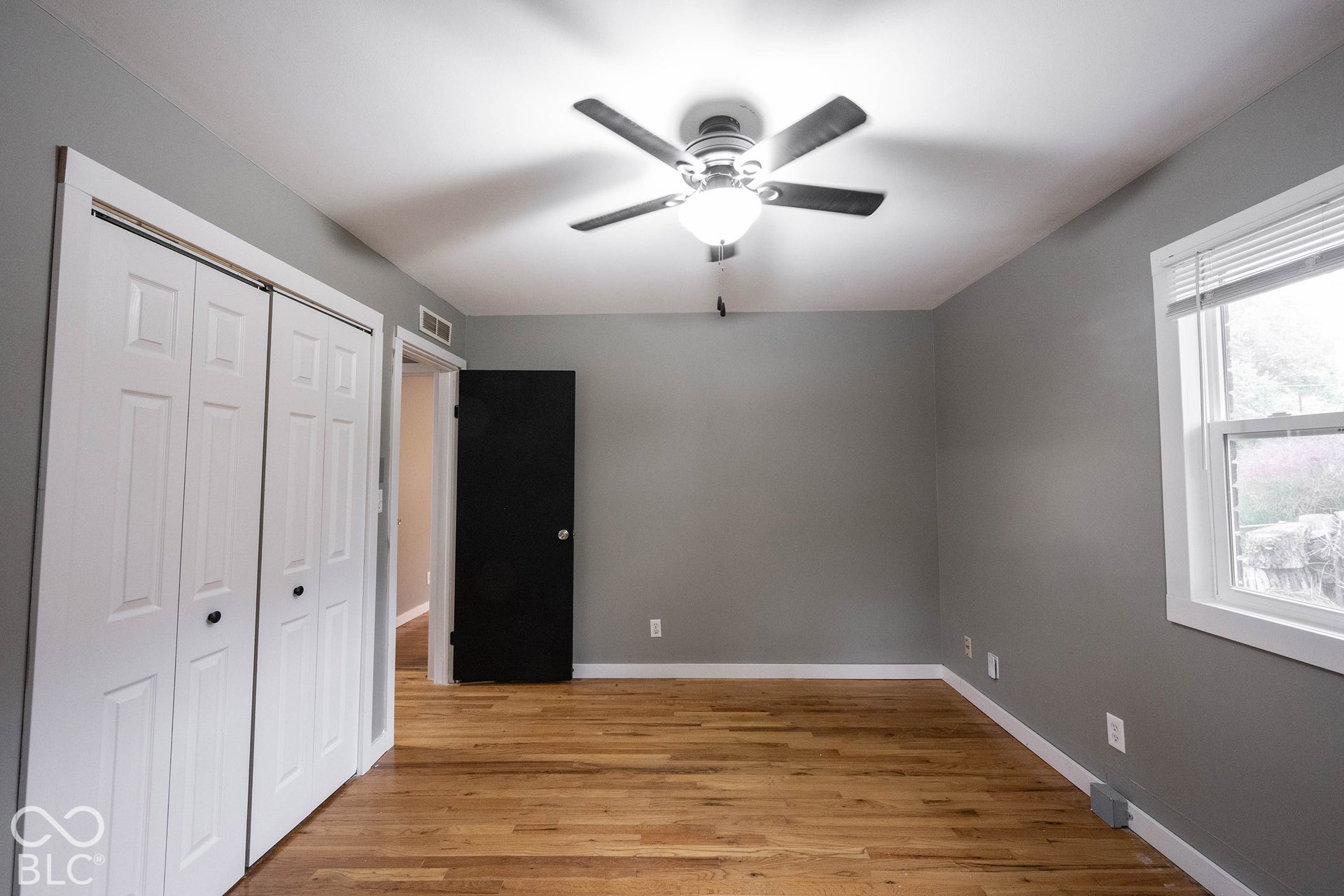 Room featuring wood-finish flooring, dual-panel closet doors, a ceiling fan with integrated lighting, and a single window with blinds