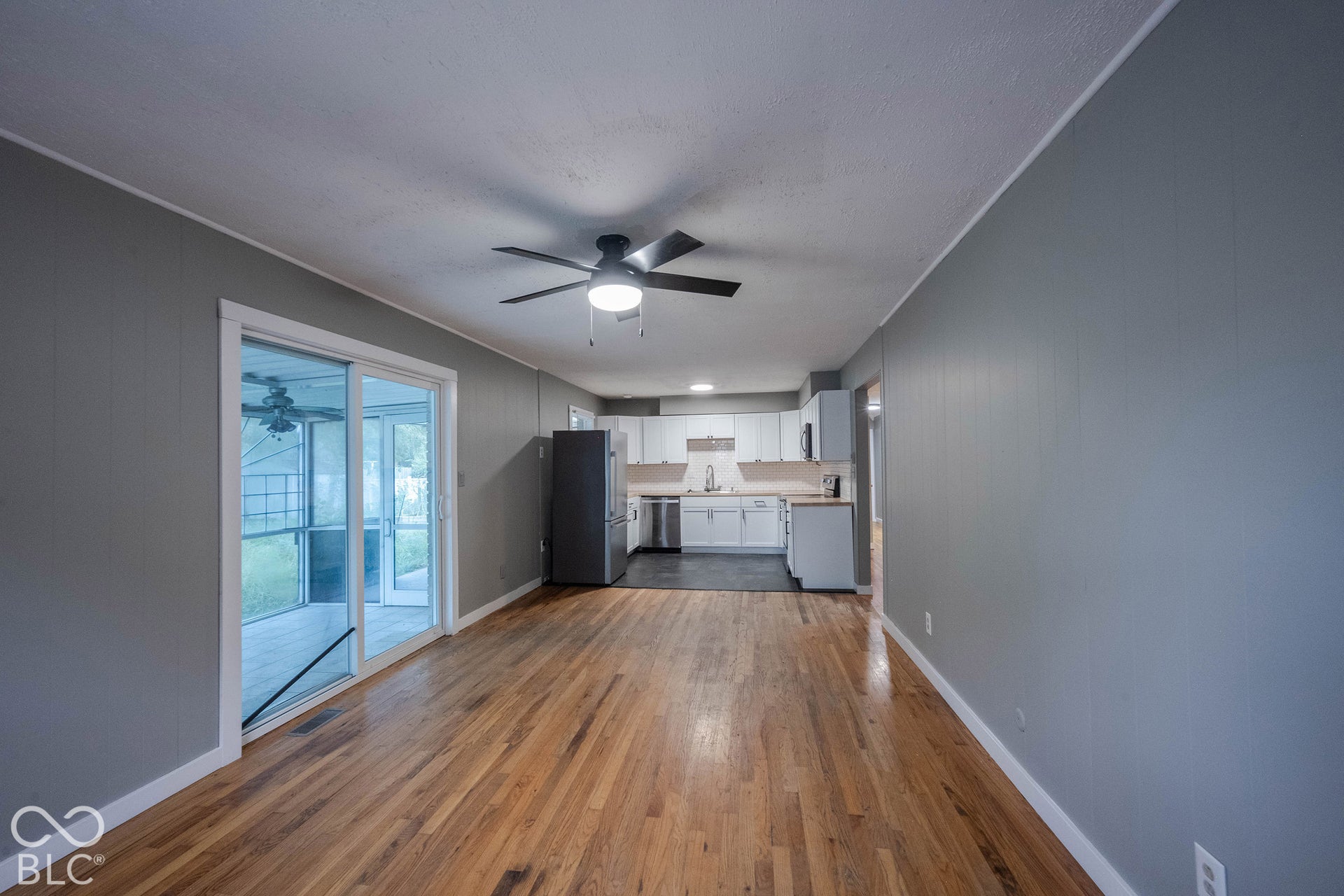 Open-concept living space featuring wood-finish flooring, white cabinetry, a sliding glass door, and a ceiling fan with integrated lighting