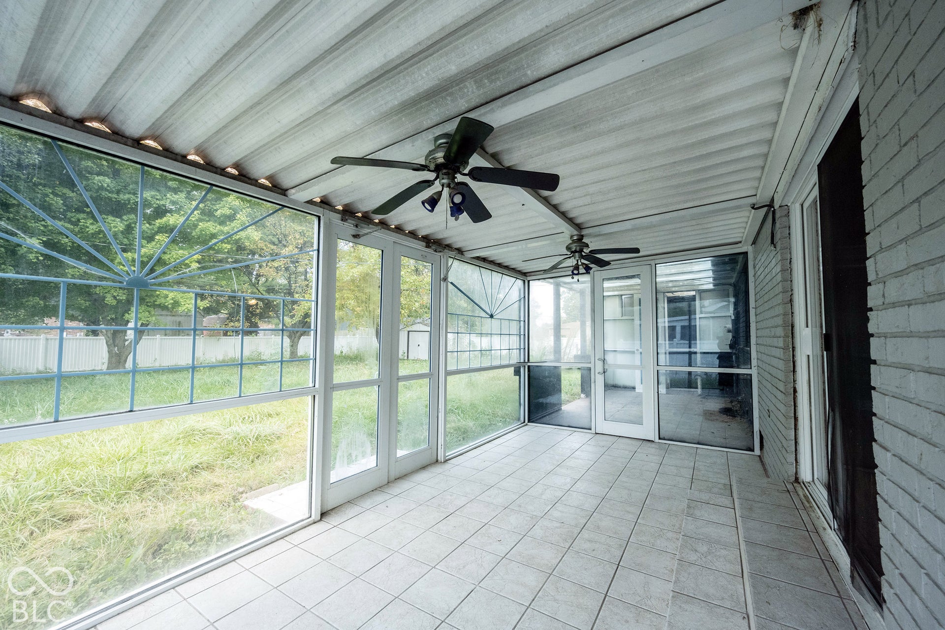 Enclosed patio featuring a corrugated metal ceiling, ceramic tile flooring, screen-enclosed walls with metal frames, and two ceiling fans
